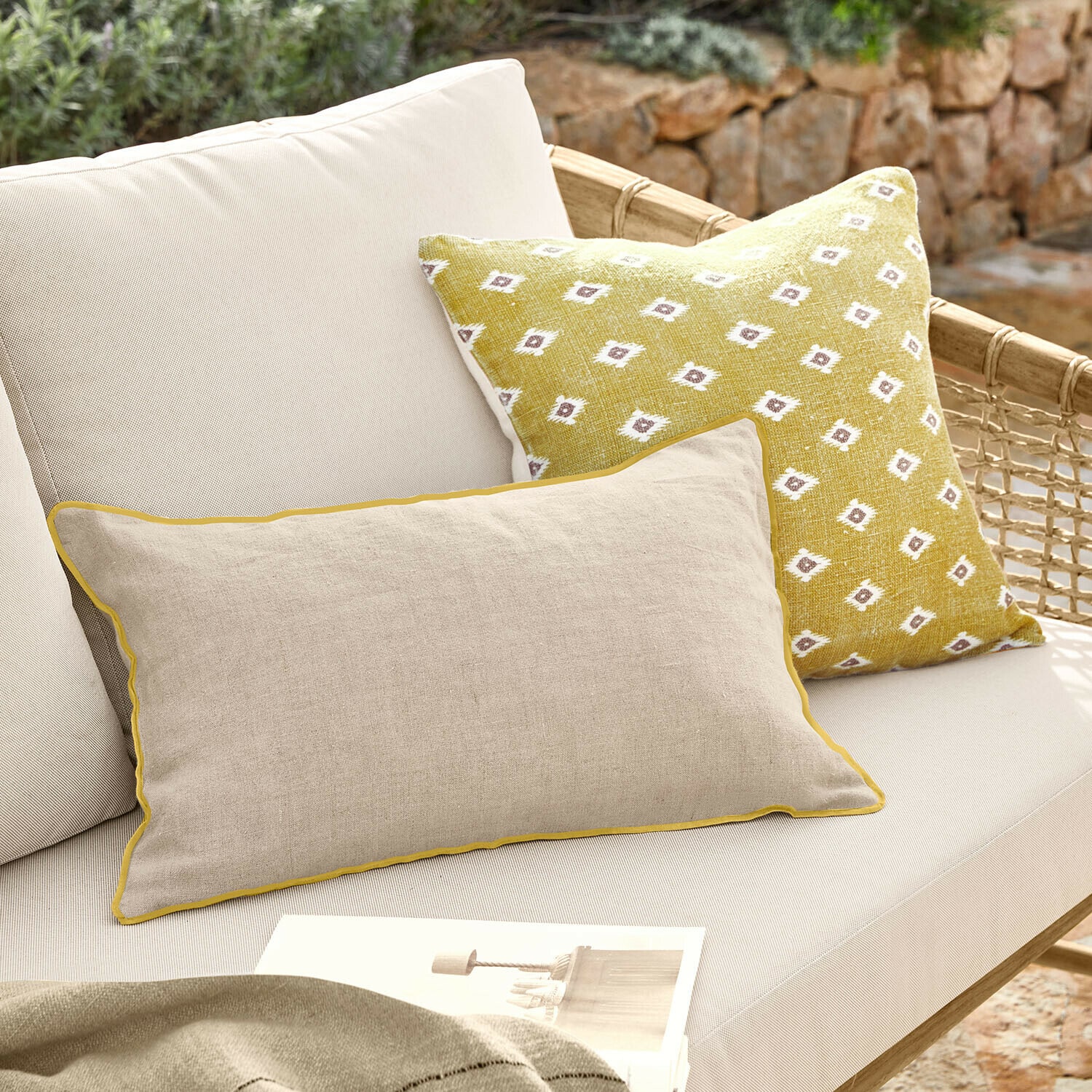 Set de 2 fundas de cojín Brisalda Cojín beige de lino con ribete amarillo y cojín amarillo con patrón blanco en sofá exterior claro