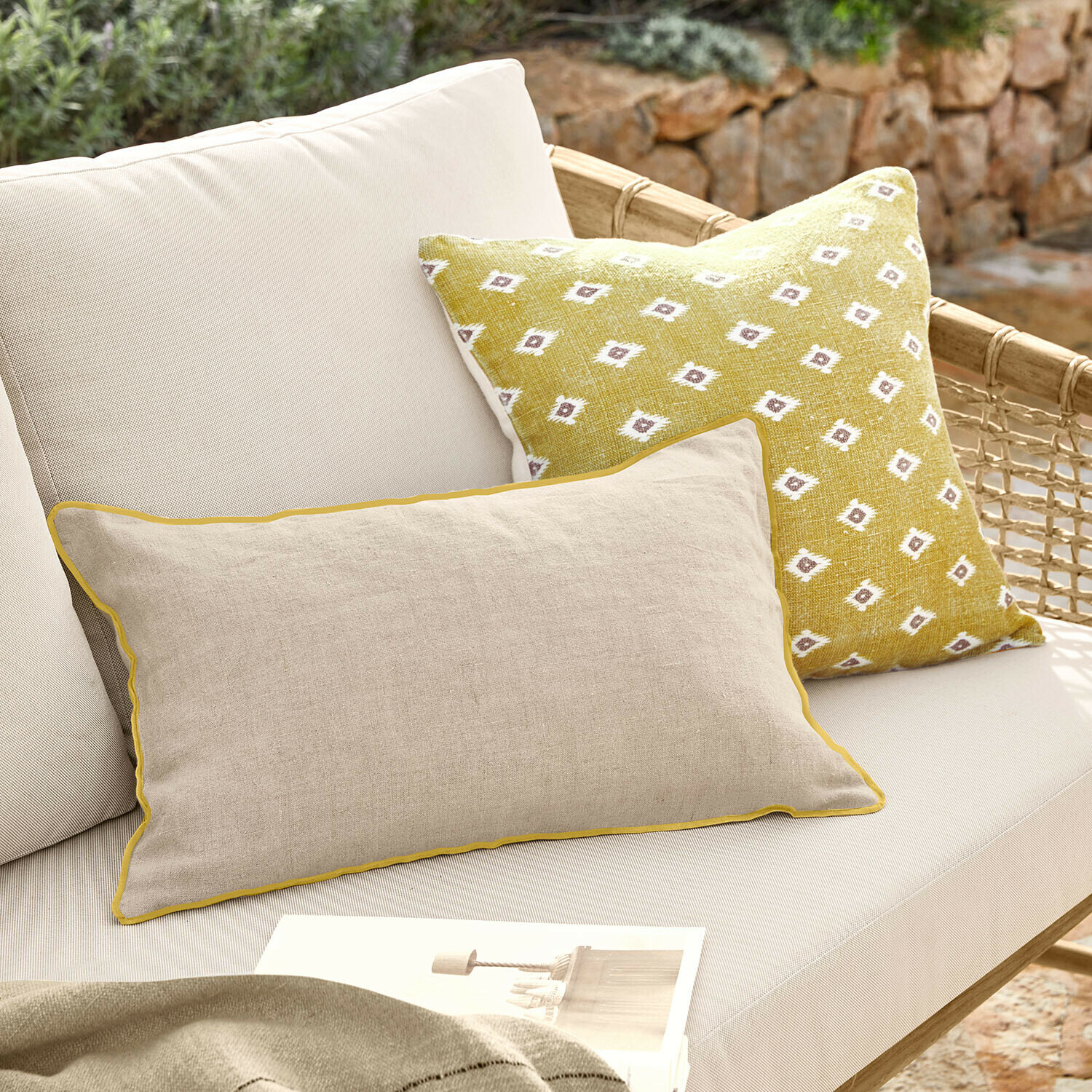Set de 2 fundas de cojín Brisalda Cojín beige de lino con ribete amarillo y cojín amarillo con patrón blanco en sofá exterior claro