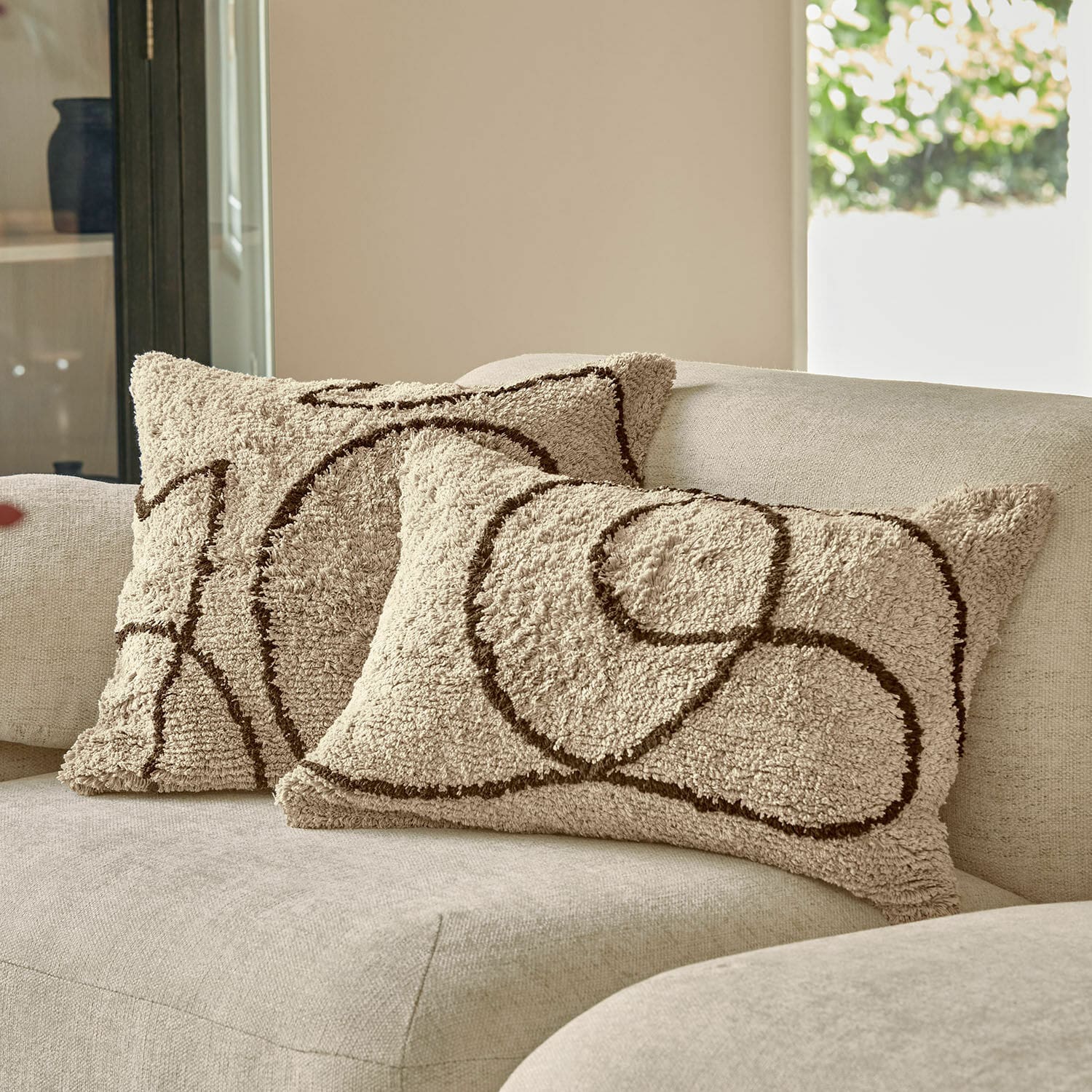 Set de 2 fundas de cojín Lavinois Cojines decorativos beige de material suave con diseño geométrico marrón sobre sofá claro