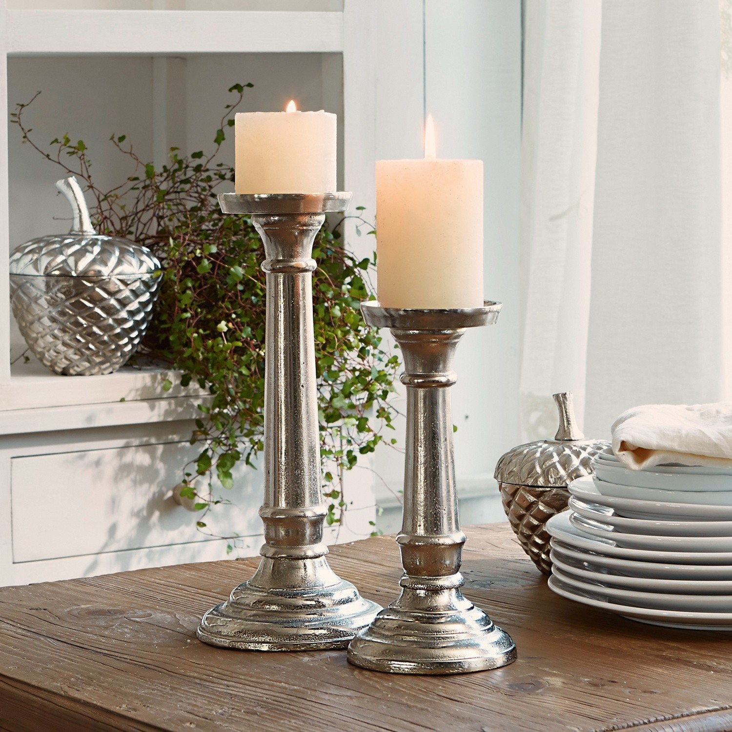 Set de 2 candeleros Symone Par de candelabros metálicos plateados con velas blancas sobre mesa de madera para decoración