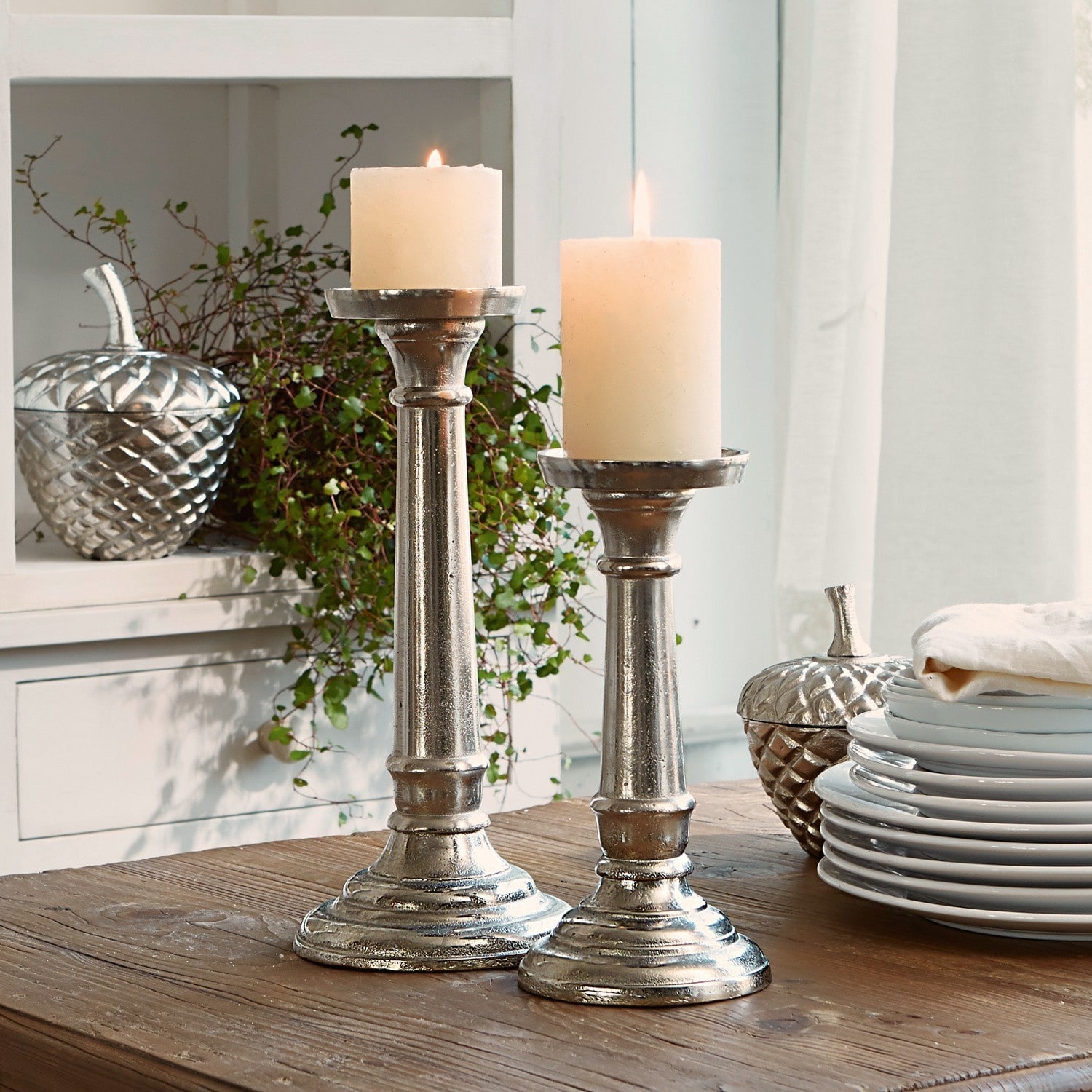 Set de 2 candeleros Symone Par de candelabros metálicos plateados con velas blancas sobre mesa de madera para decoración