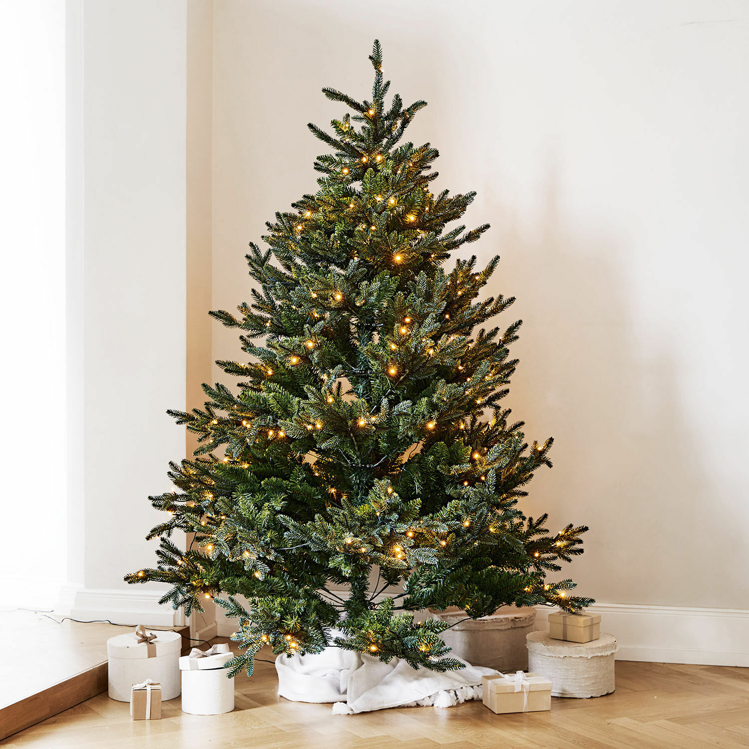 Árbol de Navidad Franck Árbol de Navidad artificial verde con luces LED cálidas sobre suelo de madera con regalos