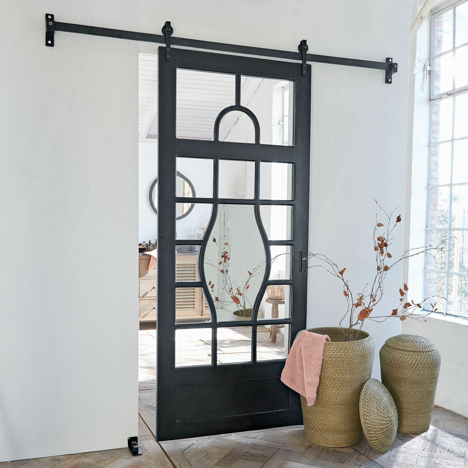 Puerta corredera Wilmorton Puerta corredera negra de metal con espejo de diseño geométrico en habitación luminosa con cestas de mimbre