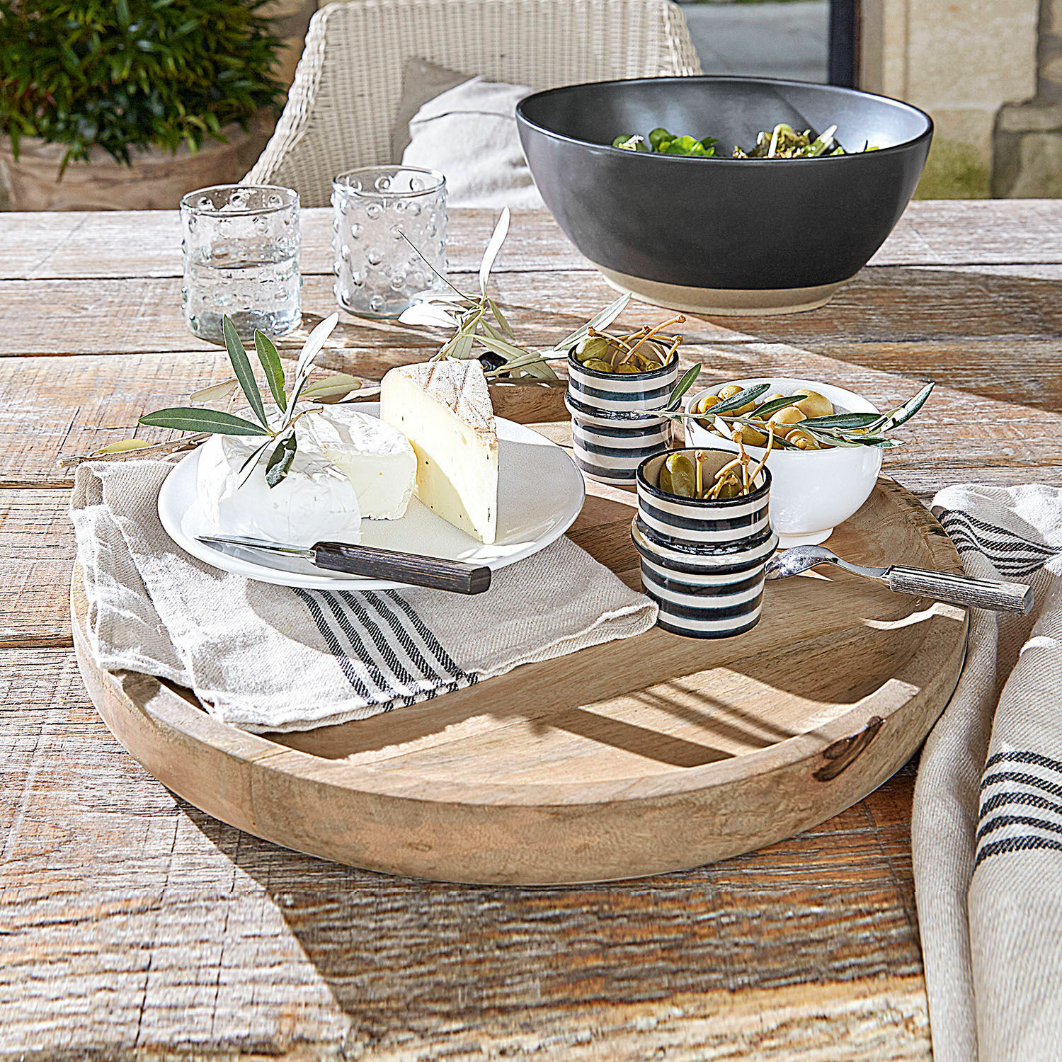 Bandeja de madera con quesos, aceitunas y tazas de cerámica sobre mesa rústica de madera