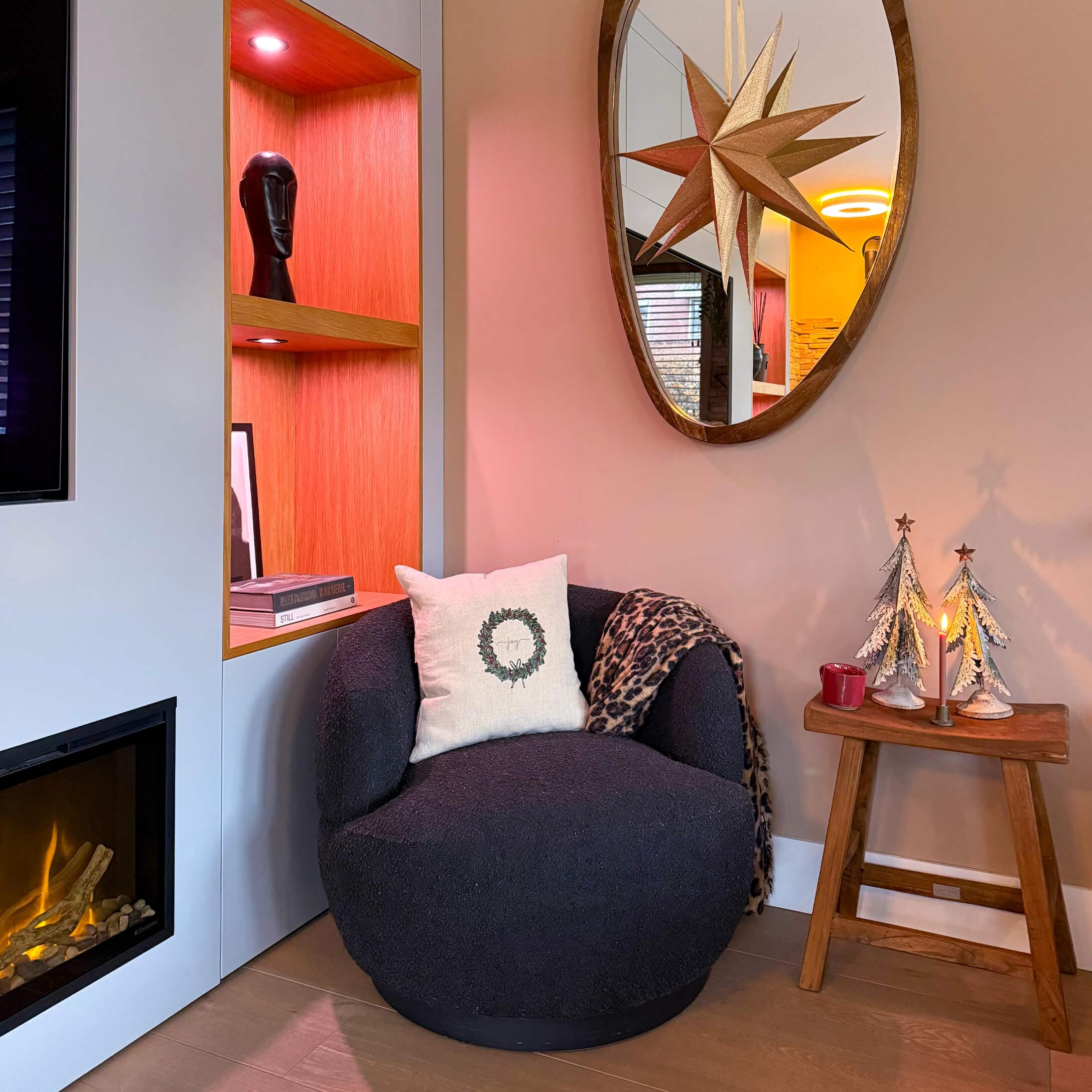 Sillón negro suave con cojín y manta junto a chimenea y mesa de madera con decoración navideña