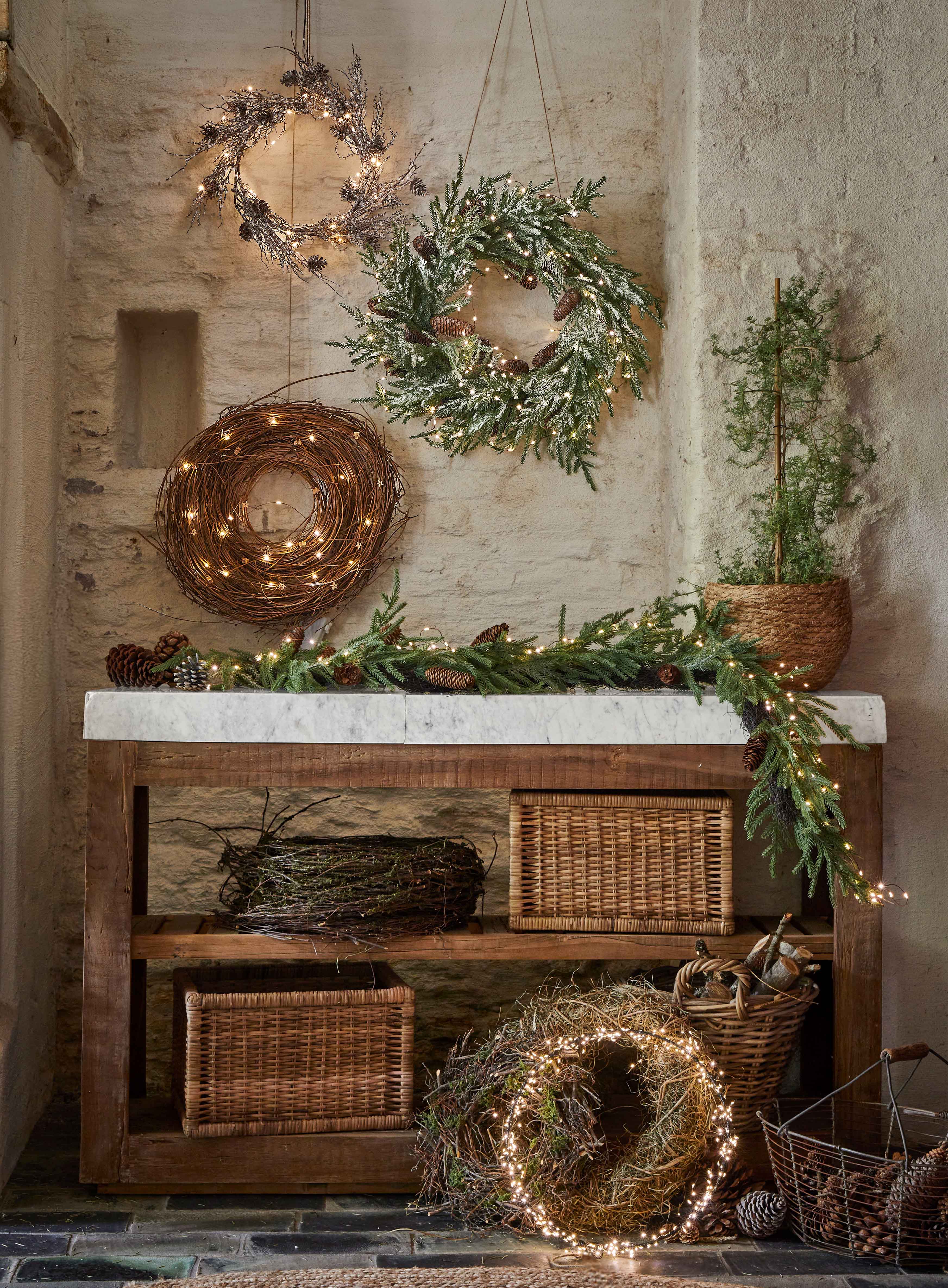 Coronas navideñas decorativas de ramas, piñas y luces sobre mesa de madera en ambiente rústico
