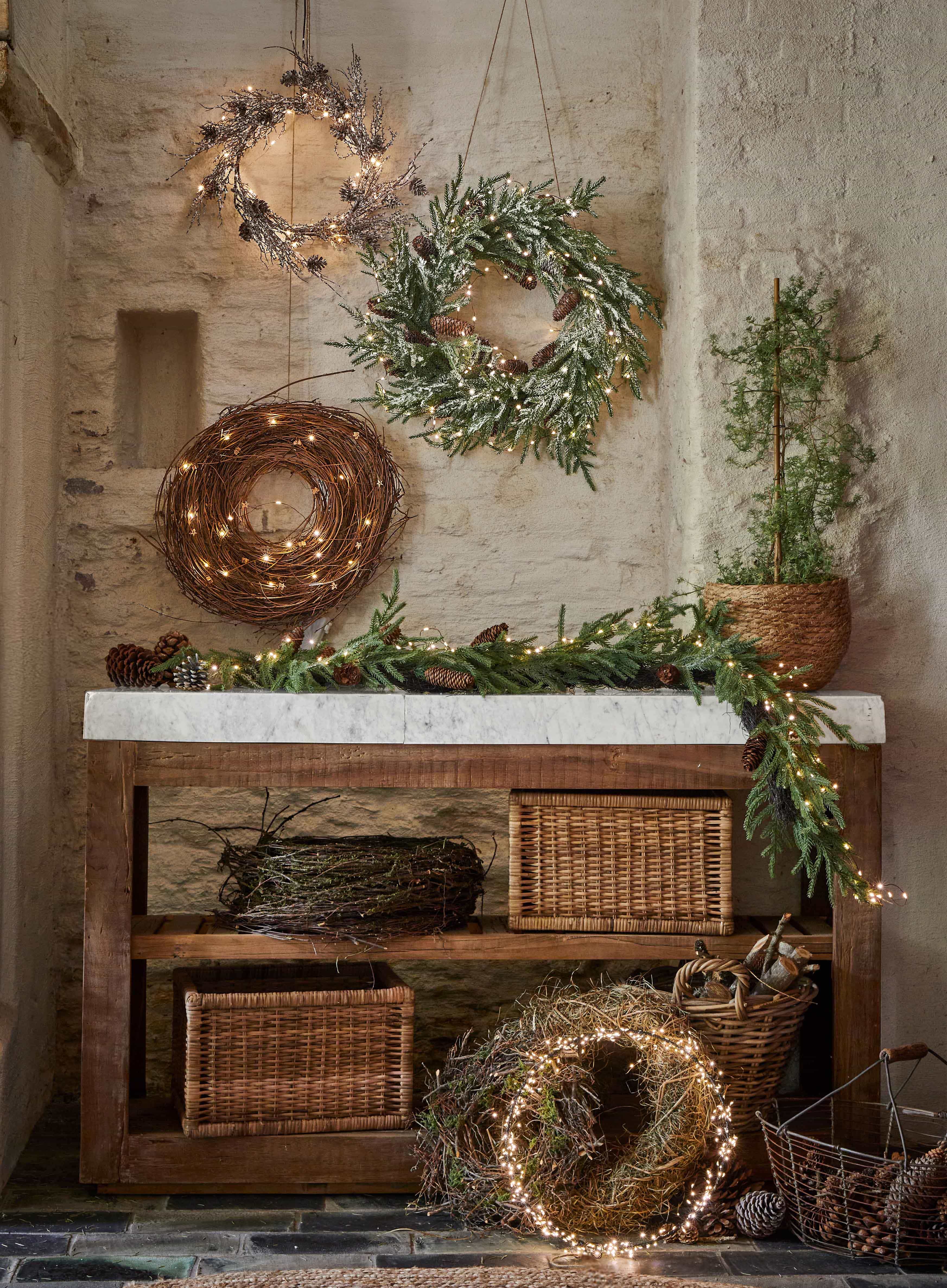 Coronas navideñas decorativas de ramas, piñas y luces sobre mesa de madera en ambiente rústico