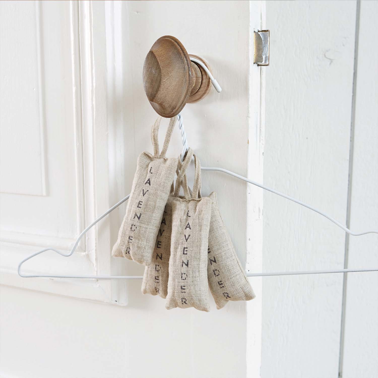 Bolsitas de lino natural con lavanda colgadas en un gancho de madera en puerta blanca