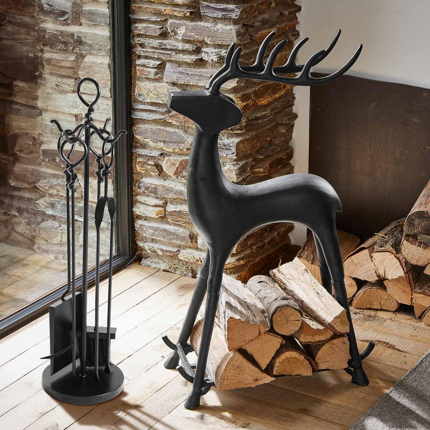 Soporte para leña de metal negro con forma de ciervo junto a herramientas de chimenea y troncos