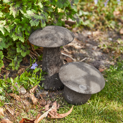 Setas decorativas de hormigón gris en jardín con césped y plantas verdes