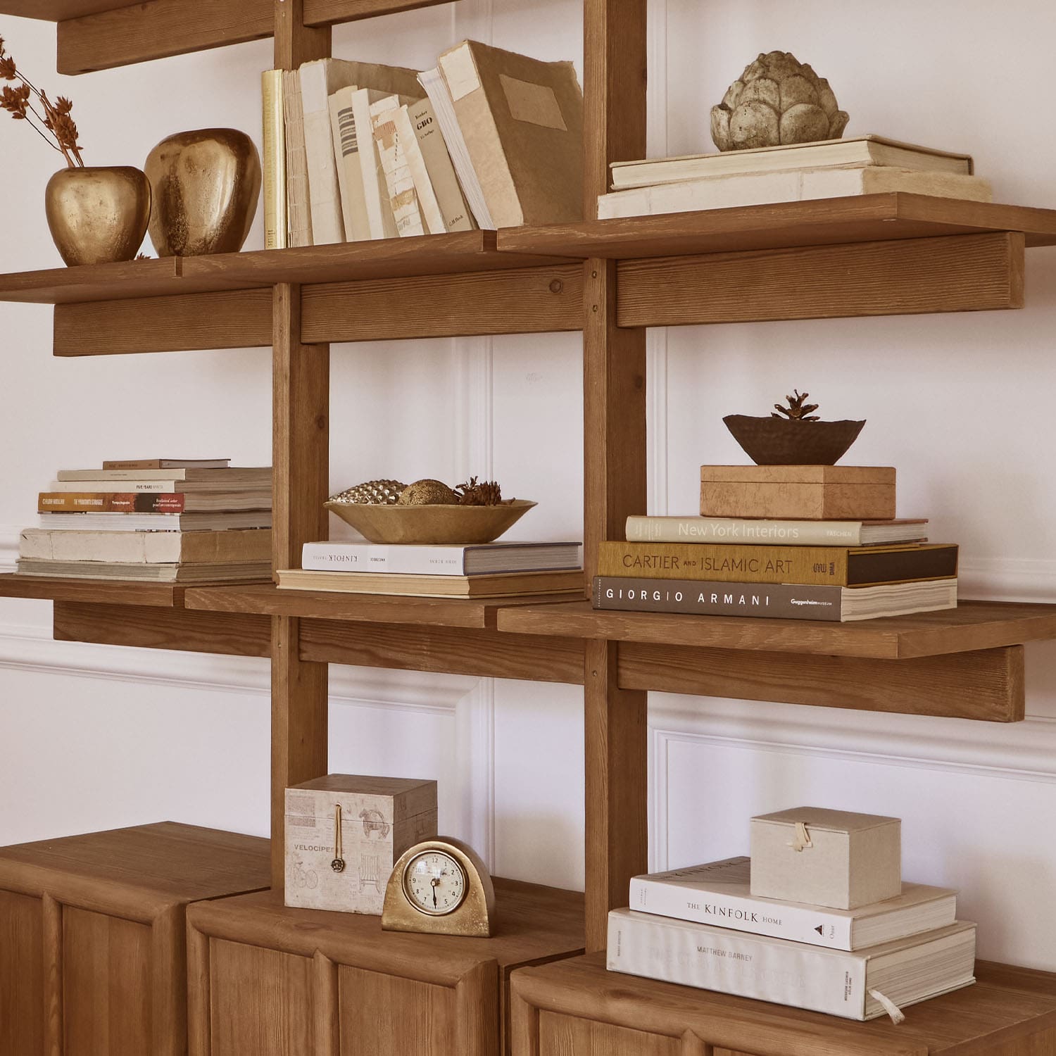 Estantería de madera con libros, decoraciones doradas y reloj, diseño interior elegante