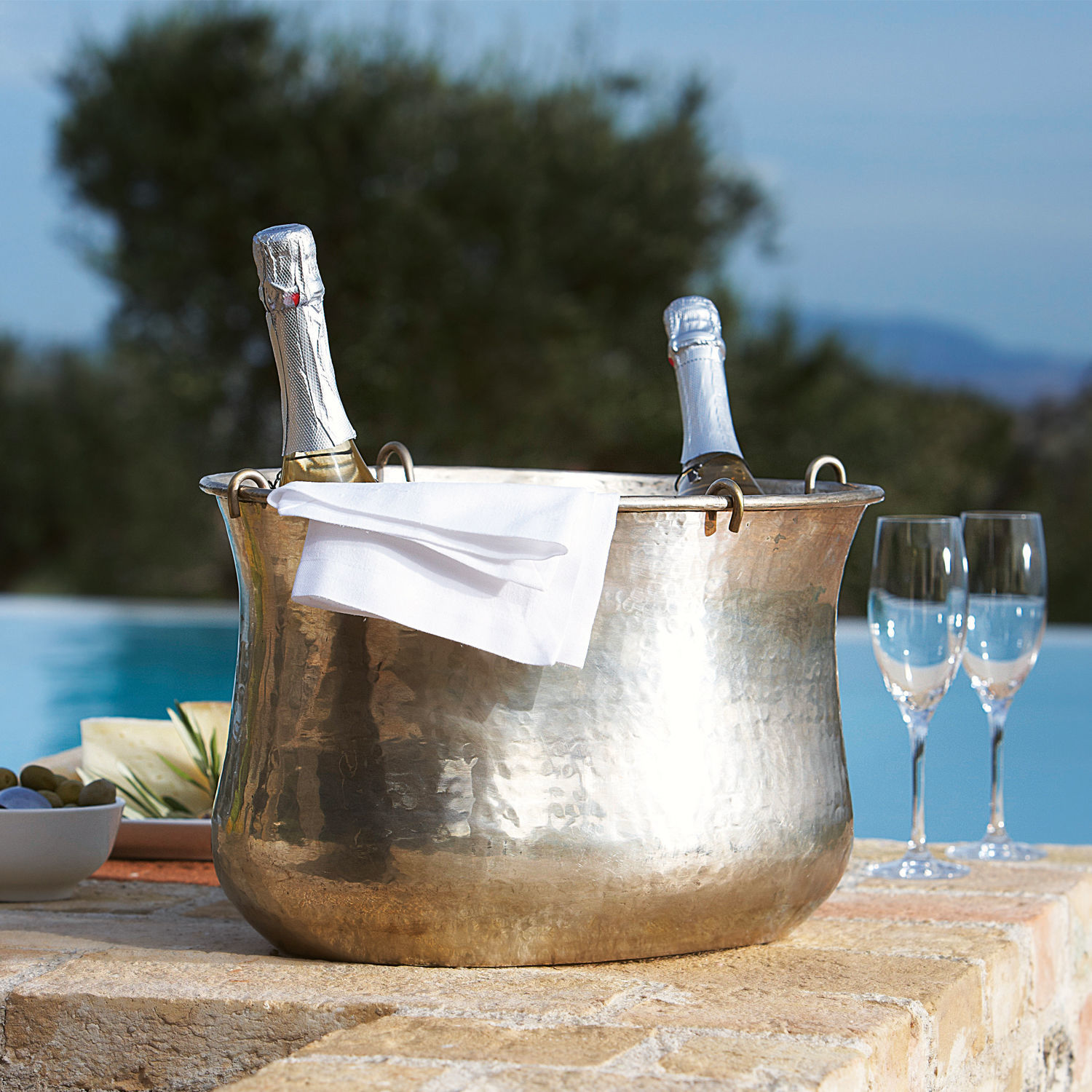 Enfriador de champán Montgomery Cubitera martillada de cobre con dos botellas de champán y servilleta blanca en terraza