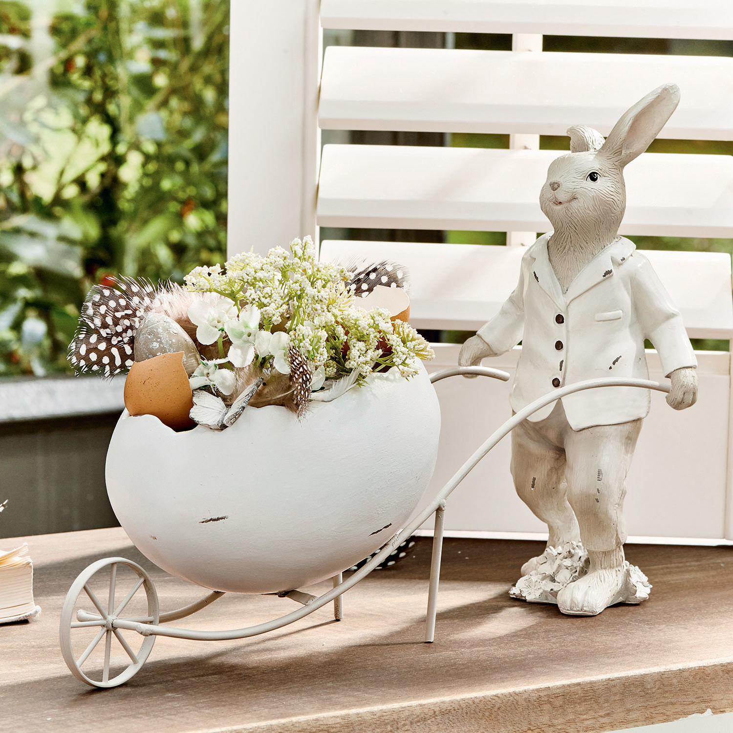 Conejo Jaris Conejo decorativo blanco con huevo de cerámica y flores en carrito metálico sobre mesa.