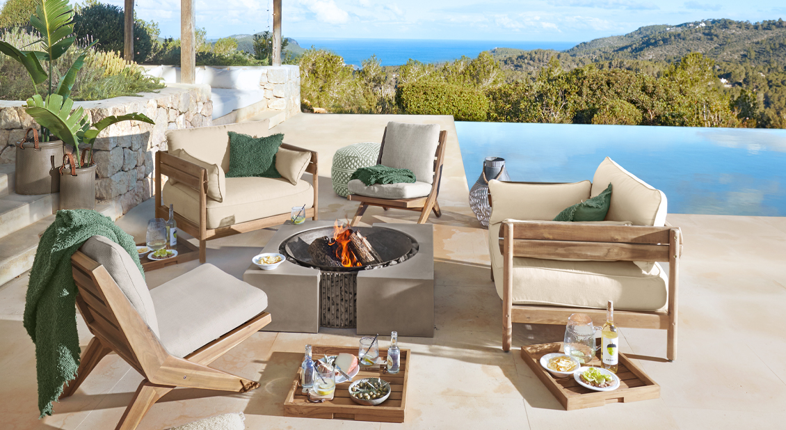 Conjunto de muebles de jardín con cojines beige y mantas verdes junto a piscina con vista al mar