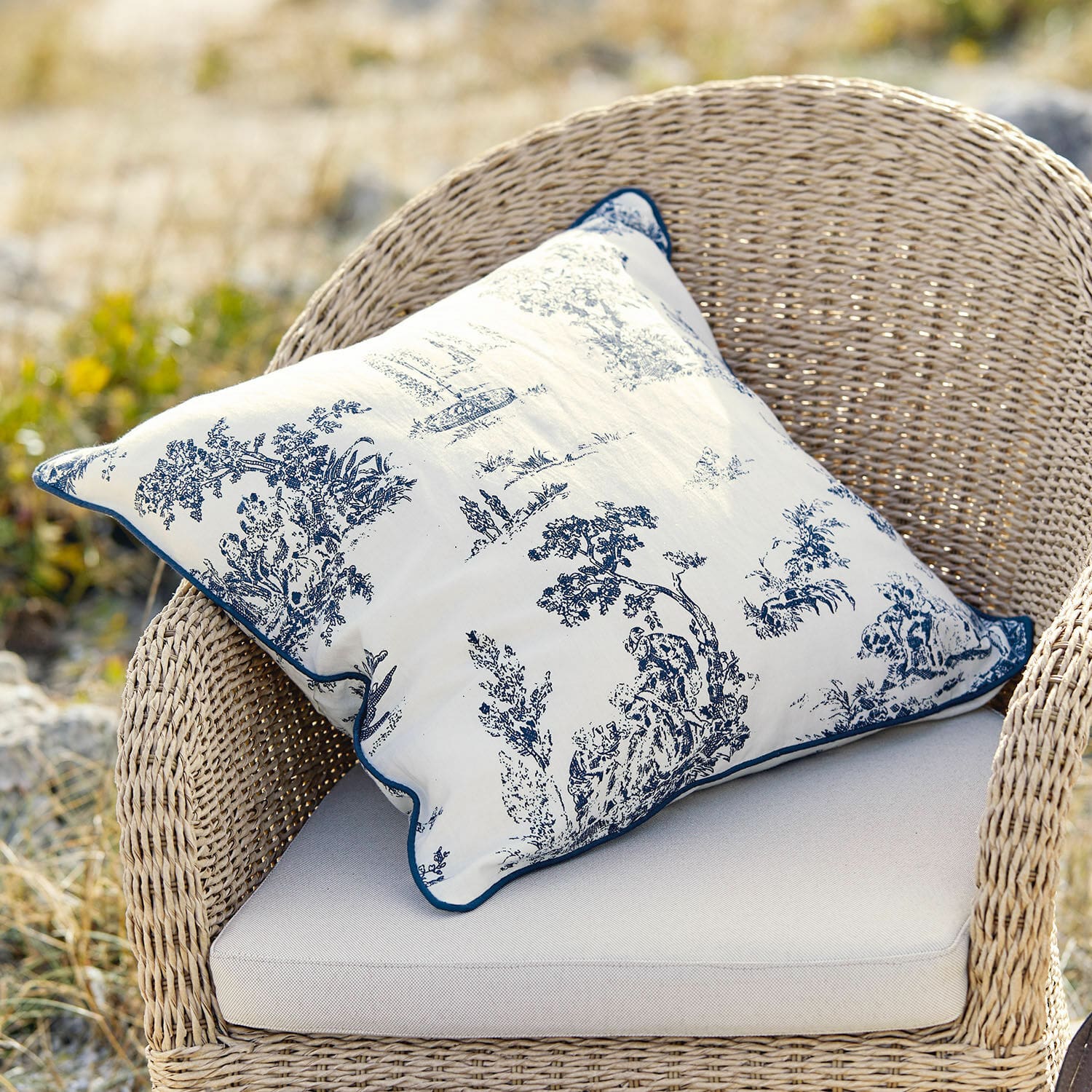 Cojín decorativo de algodón blanco con diseño clásico azul sobre silla de mimbre