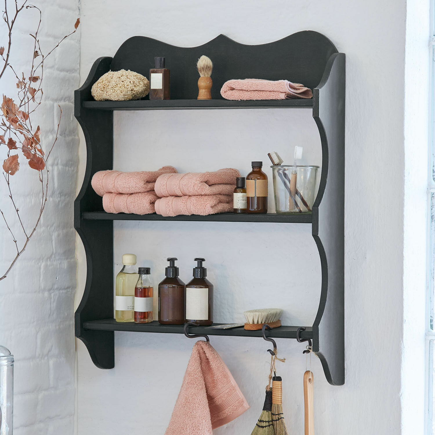 Estante de madera negro con toallas rosas y accesorios de cuidado personal en baño