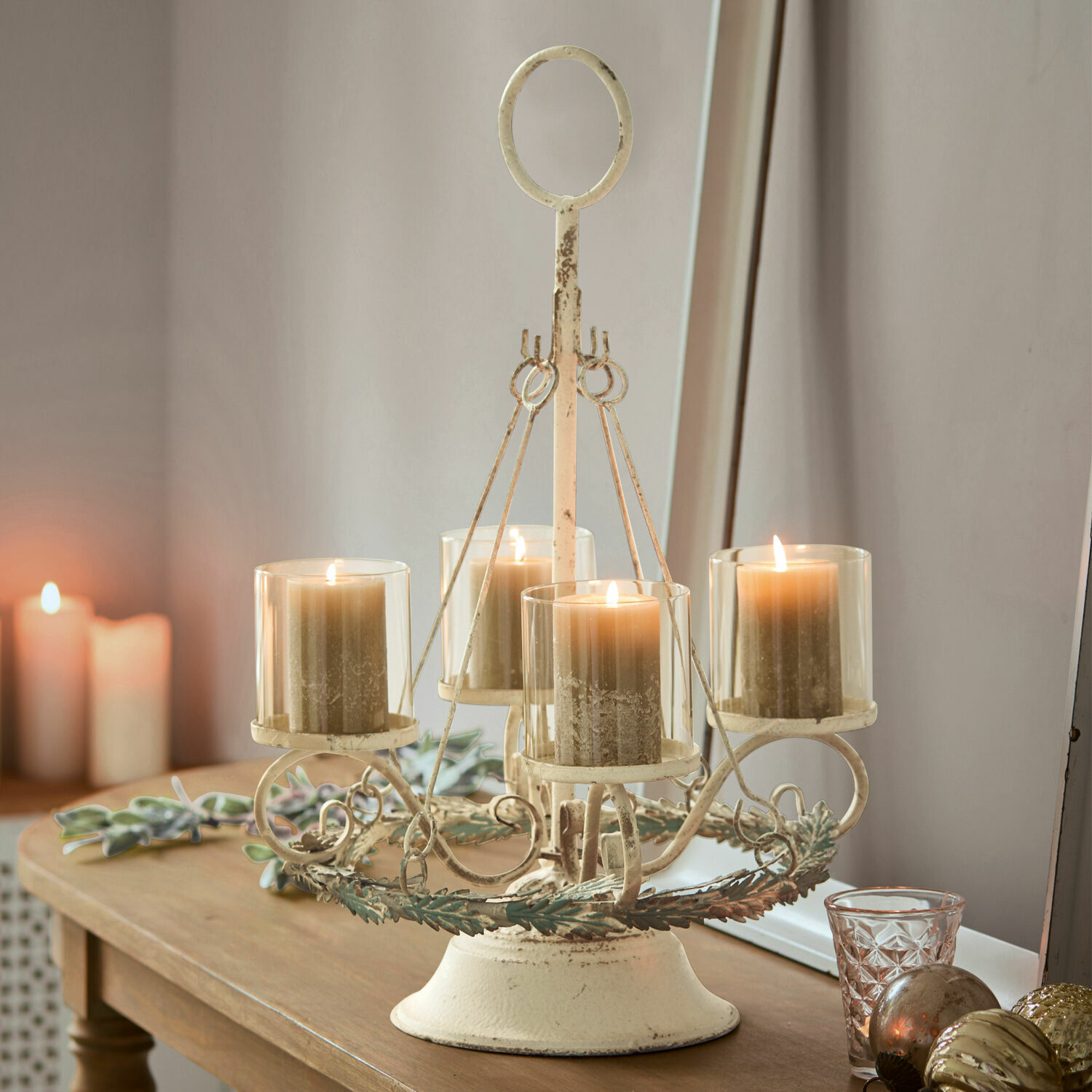 Candelabro metálico vintage color crema con cuatro velas beige sobre mesa de madera, decoración