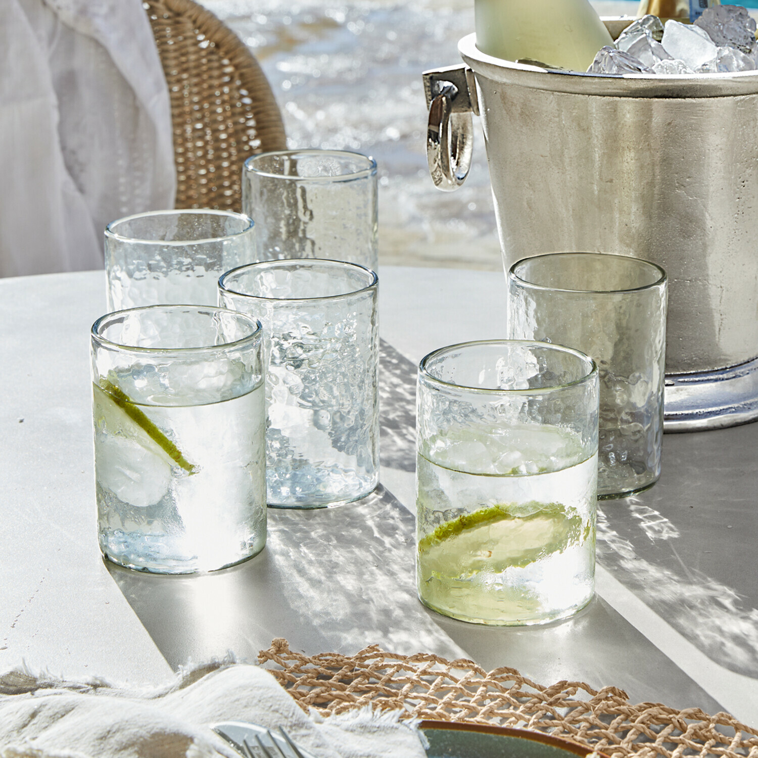 Vasos de vidrio transparente con textura, dos con rodajas de lima y hielo sobre mesa blanca