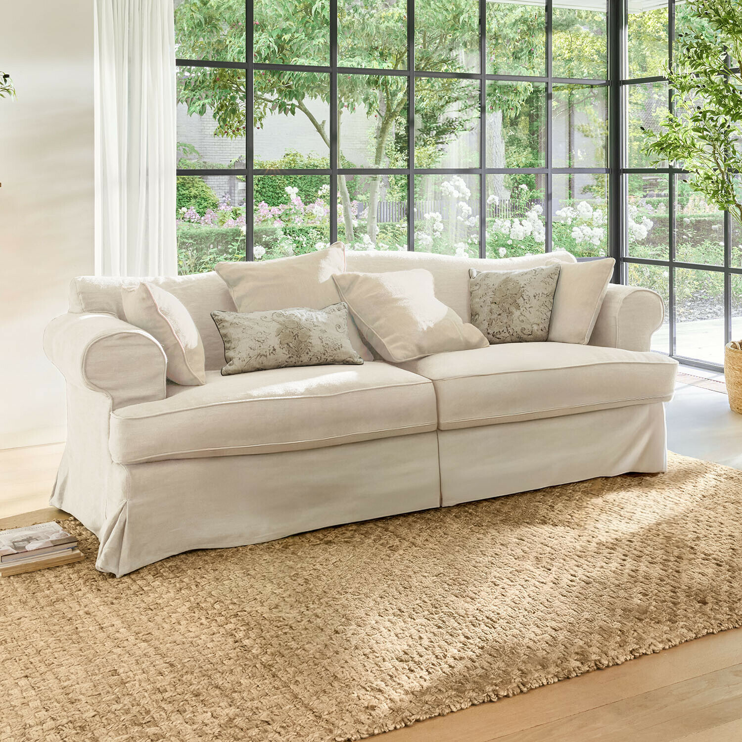 Sofá Dawnhurst Sofá beige de tela con cojines decorativos sobre alfombra natural en salón luminoso con grandes ventanas