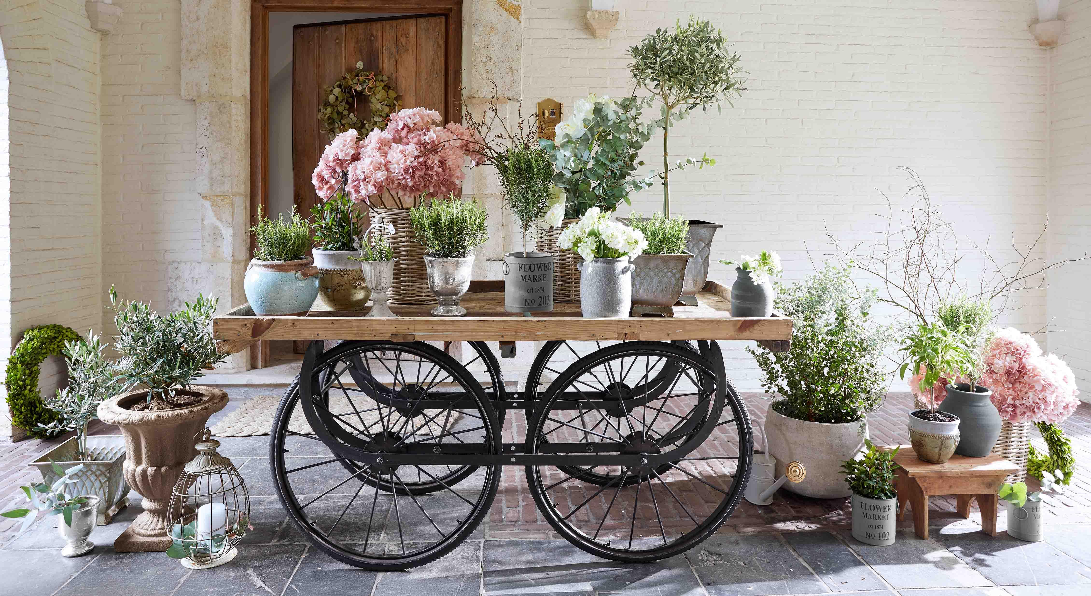Carro de madera con ruedas negras y macetas con flores rosas y blancas variadas