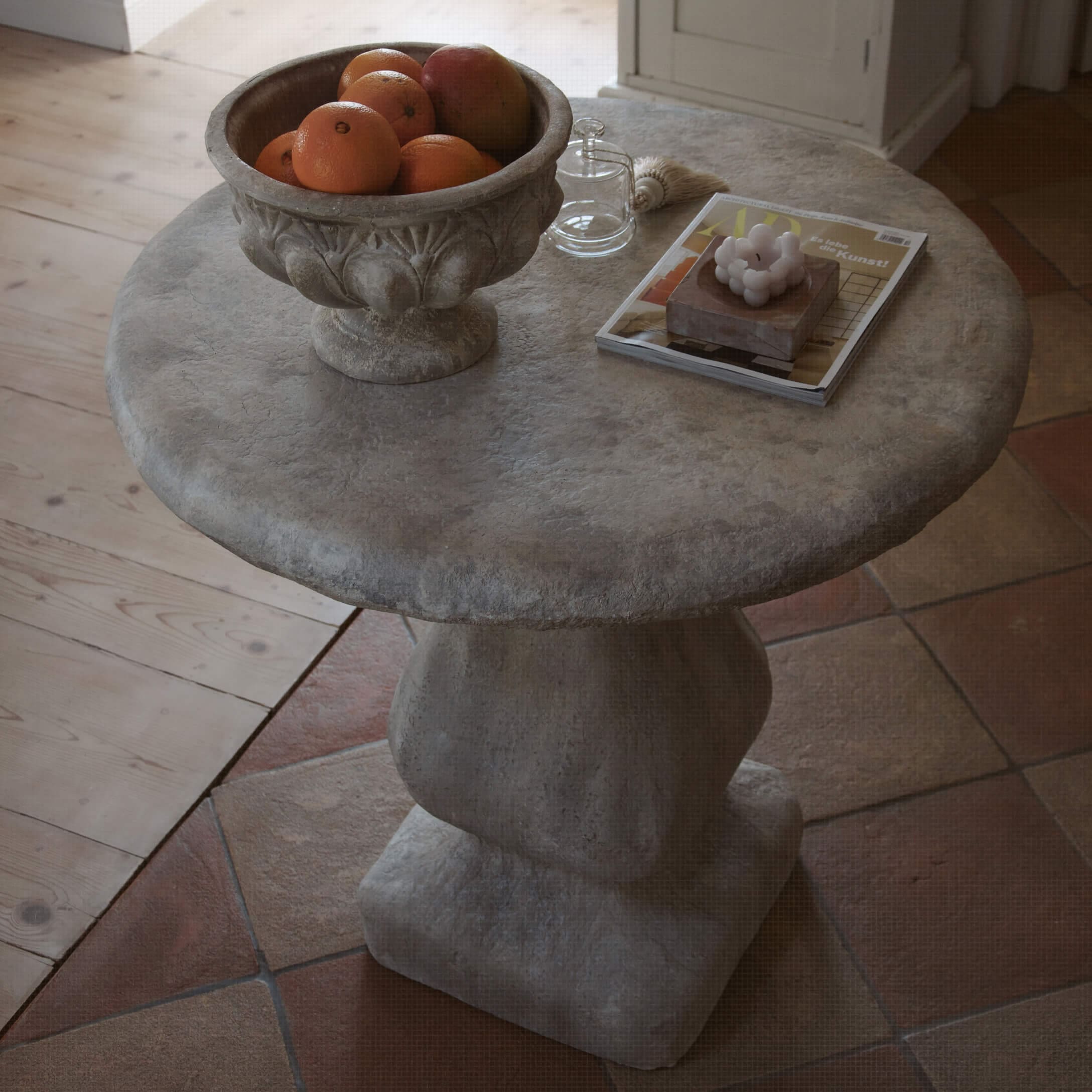 Mesa redonda de piedra gris con cuenco de frutas y objetos decorativos sobre la superficie