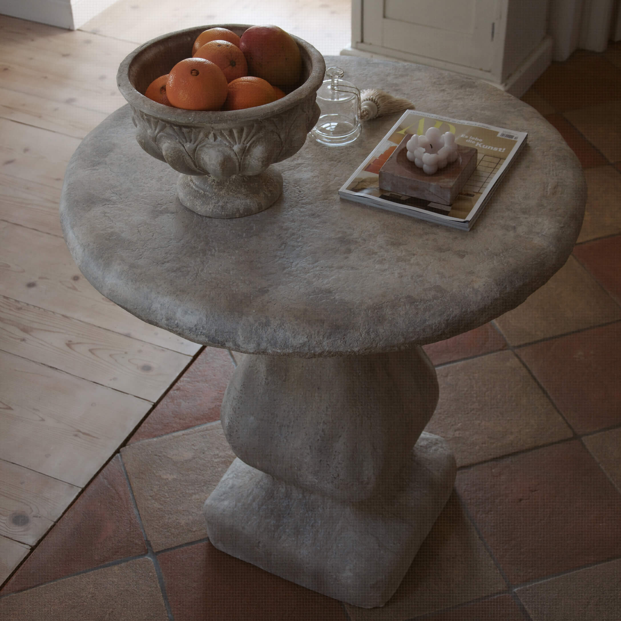 Mesa redonda de piedra gris con cuenco de frutas y objetos decorativos sobre la superficie