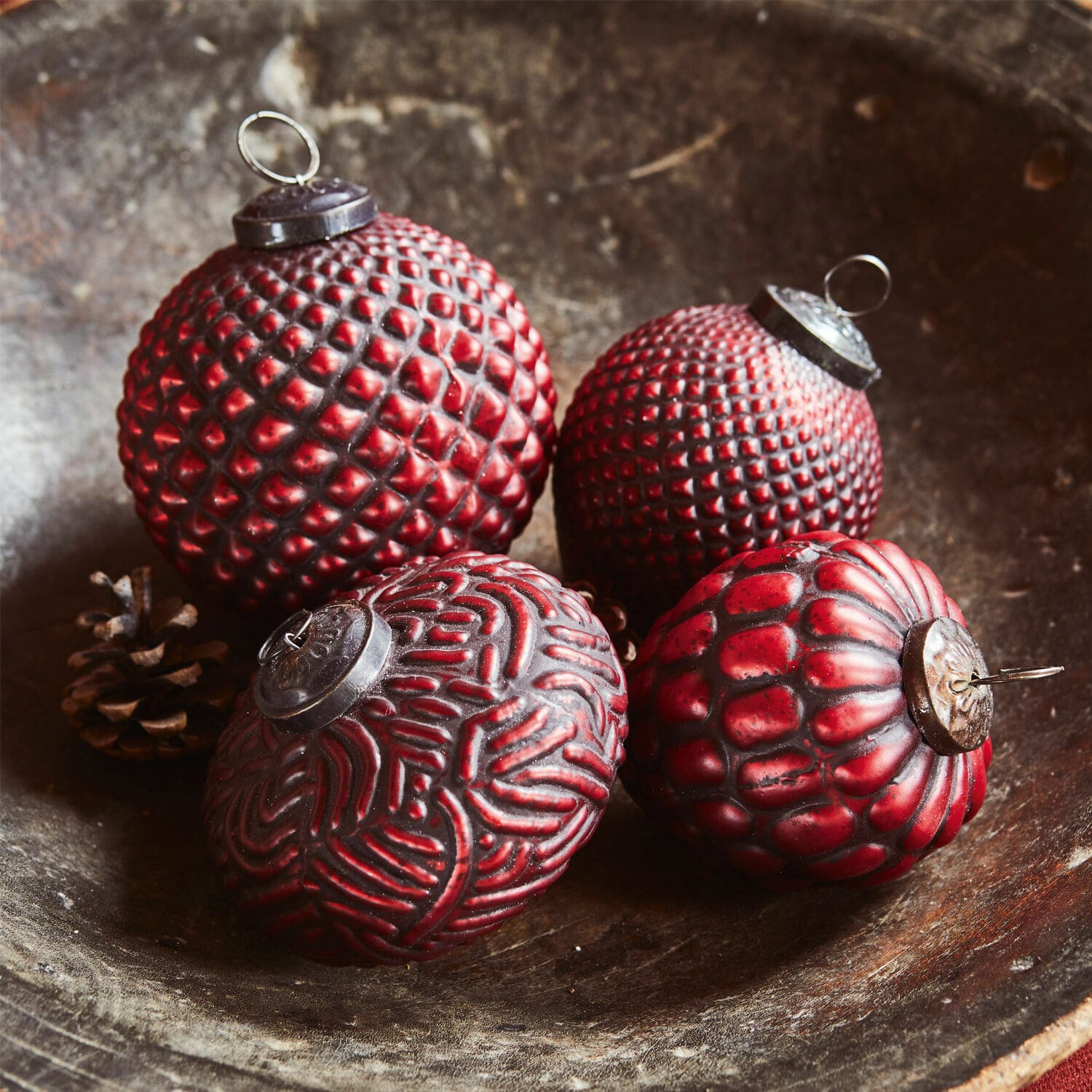 Set de 4 adornos navideños Meyen Cuatro bolas navideñas rojas con texturas variadas en un cuenco de madera, decoración festiva