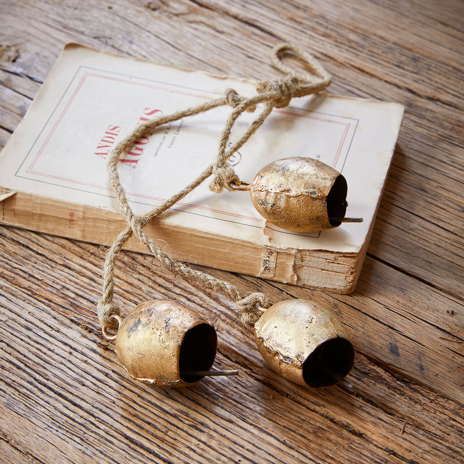 Set de 3 campanas Orelli Tres campanas metálicas doradas en cuerda sobre mesa de madera con libro antiguo
