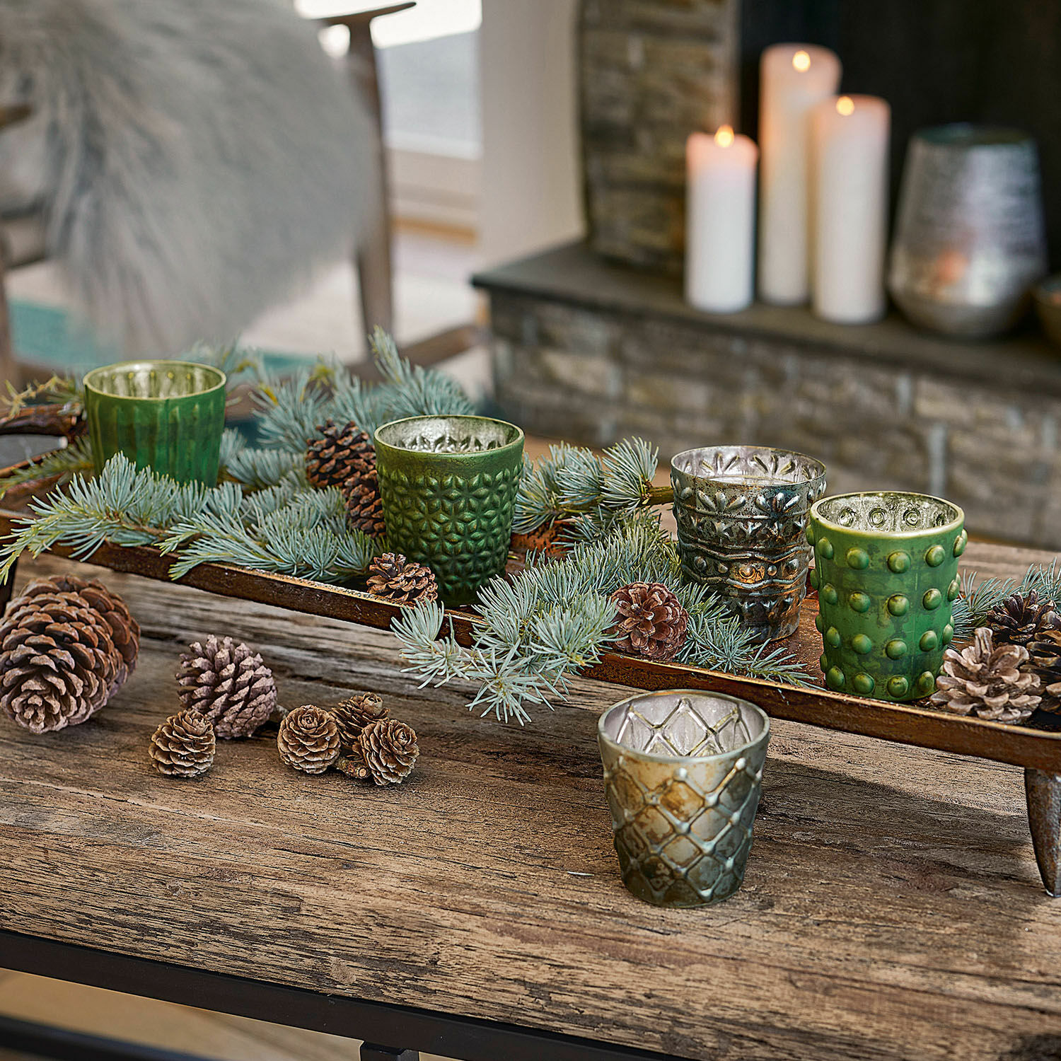 Set de 5 linternas Morazan Portavelas de vidrio verde y plateado con ramas y piñas sobre mesa de madera rústica