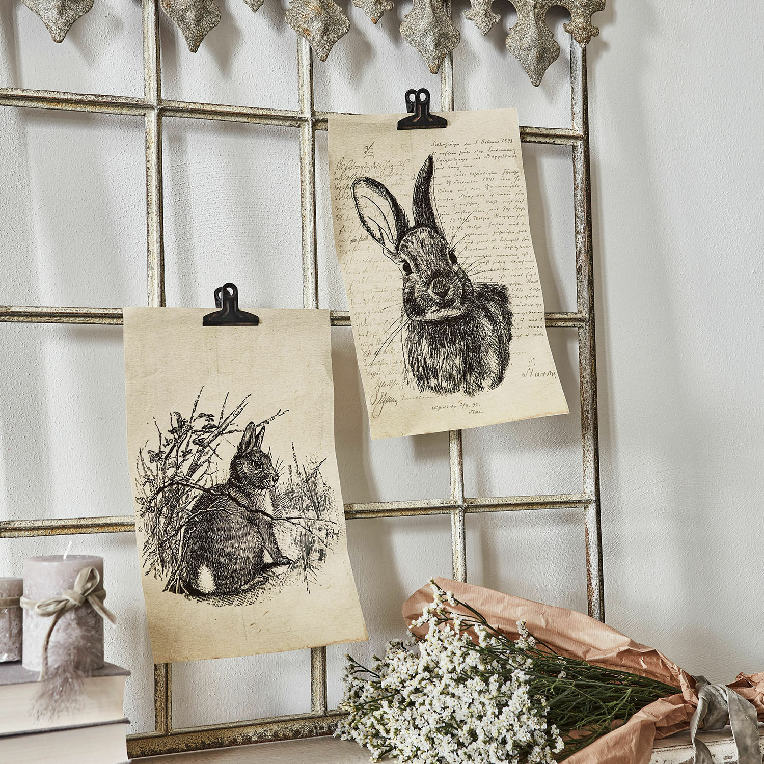 Set de 2 cuadros Meursault Dos dibujos de conejos en papel sujetos a una rejilla metálica con flores blancas y velas al lado