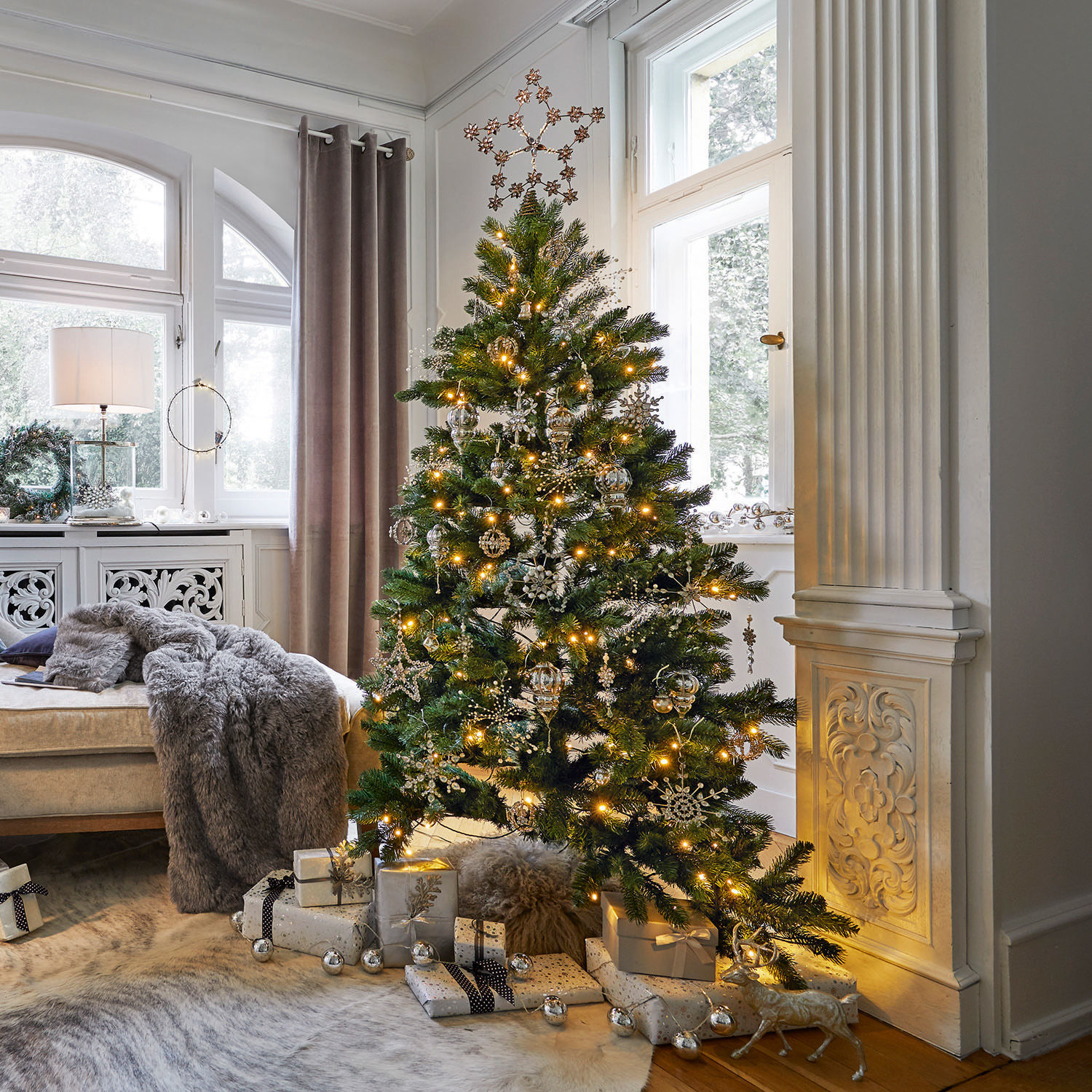Árbol de Navidad Helford Árbol de Navidad verde con adornos dorados y luces en sala luminosa con regalos debajo