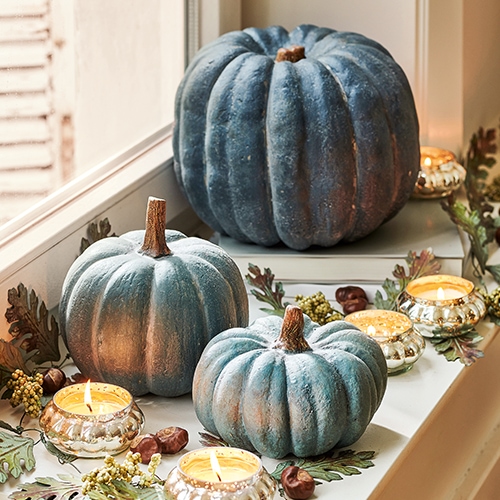 Calabazas decorativas azuladas en el alféizar con velas encendidas y hojas otoñales