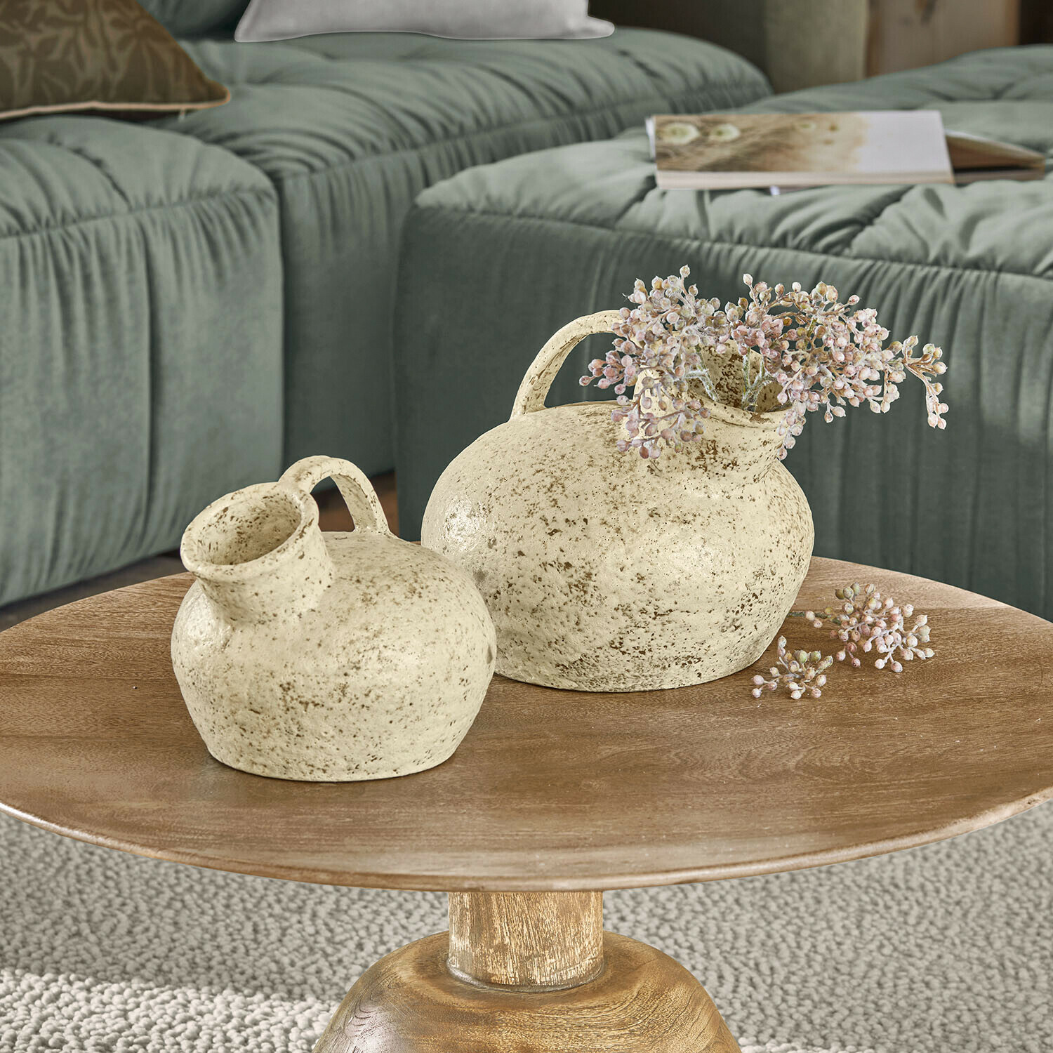 Vase 2er Set Gravière Dos jarrones de cerámica crema con asas sobre mesa de madera frente a sofá verde en sala de estar