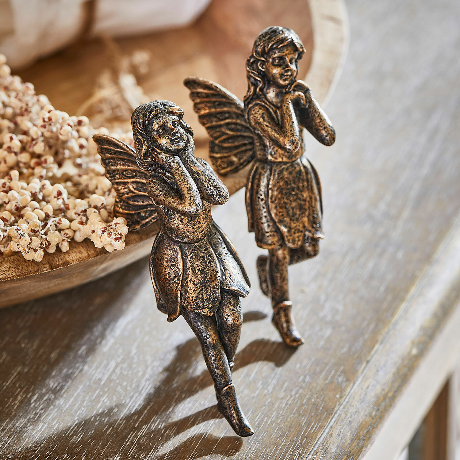 Dos figuras decorativas de hadas de metal en color dorado envejecido sobre mesa de madera, decoración