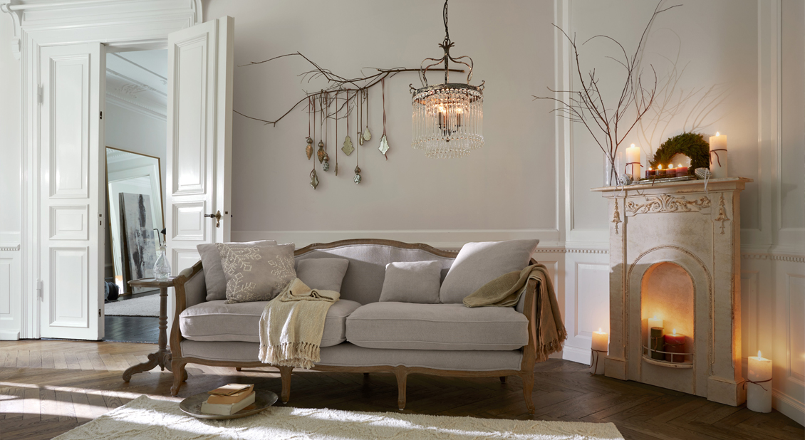 Sofá estilo francés beige con estructura de madera en salón elegante con chimenea y velas decorativas