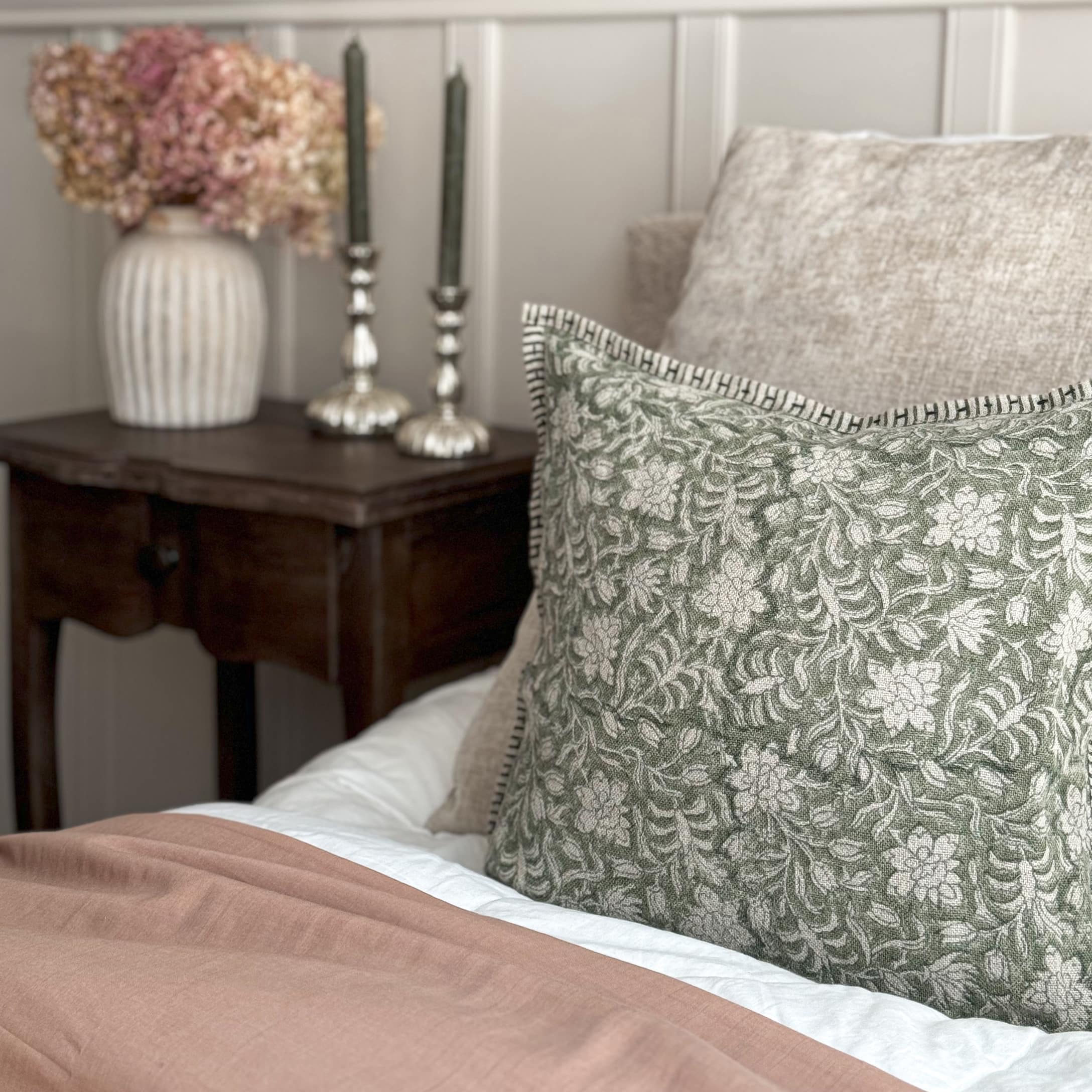 Cojín decorativo verde con patrón floral sobre tela beige en cama de estilo vintage