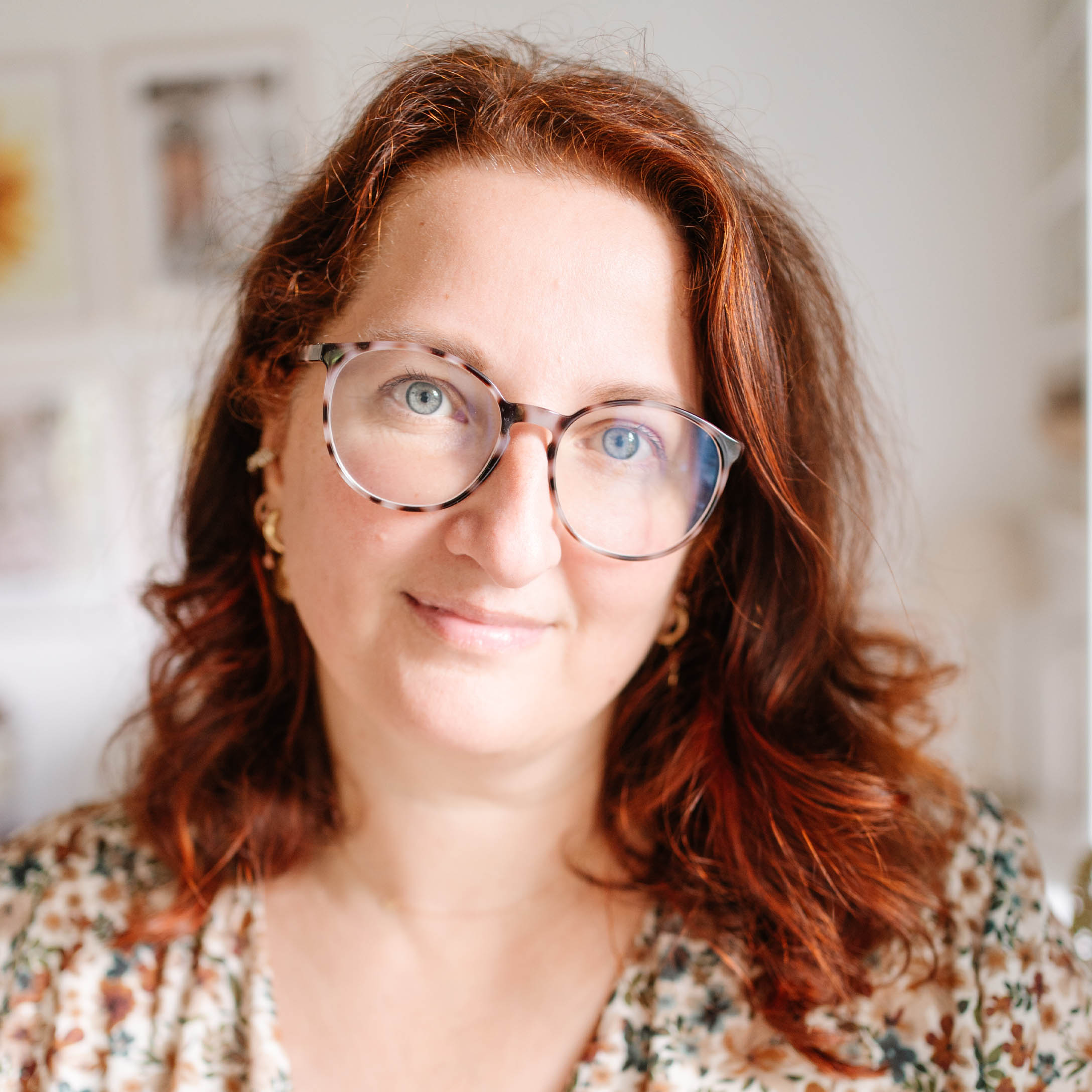 Retrato de mujer con cabello rojo y gafas con blusa floral en interior luminoso