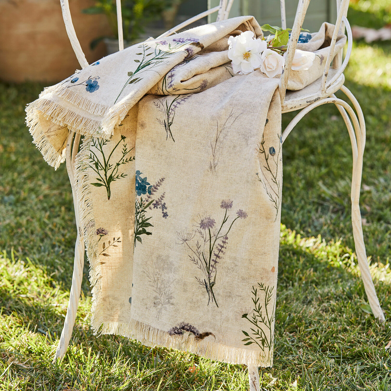 Plaid Cabinda Mantel de lino beige con estampado floral y flecos sobre silla metálica blanca en jardín