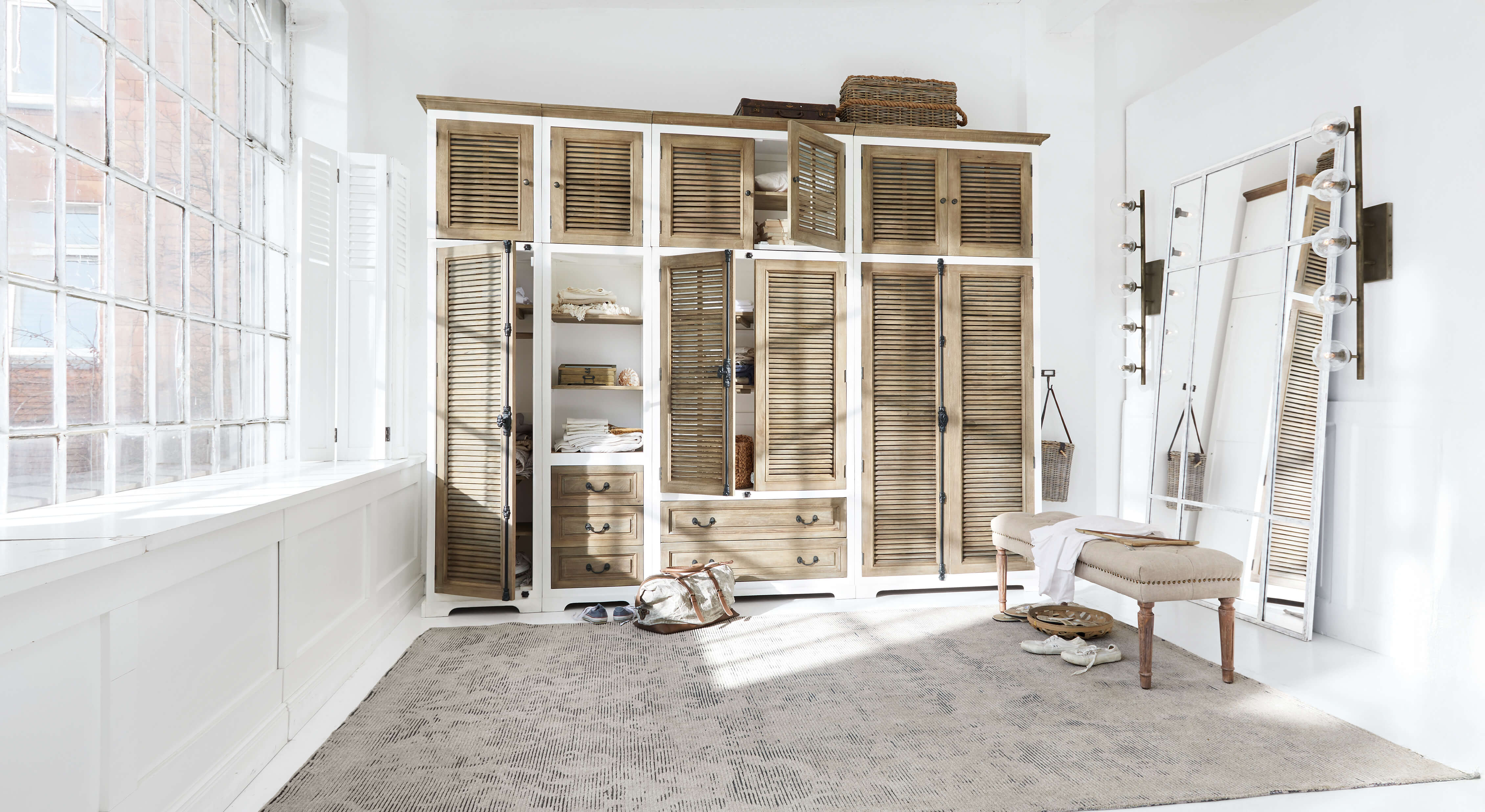 Amplio armario de madera blanca y natural con puertas de persiana y gran espejo en habitación luminosa