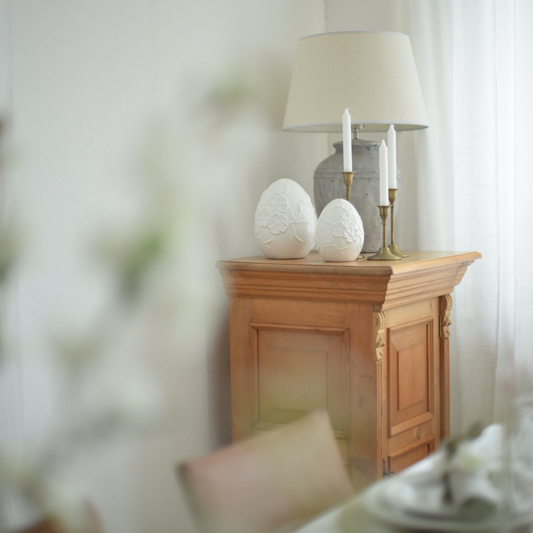 Mueble de madera con lámpara, velas y decoraciones de cerámica blanca en forma de huevos en interior luminoso