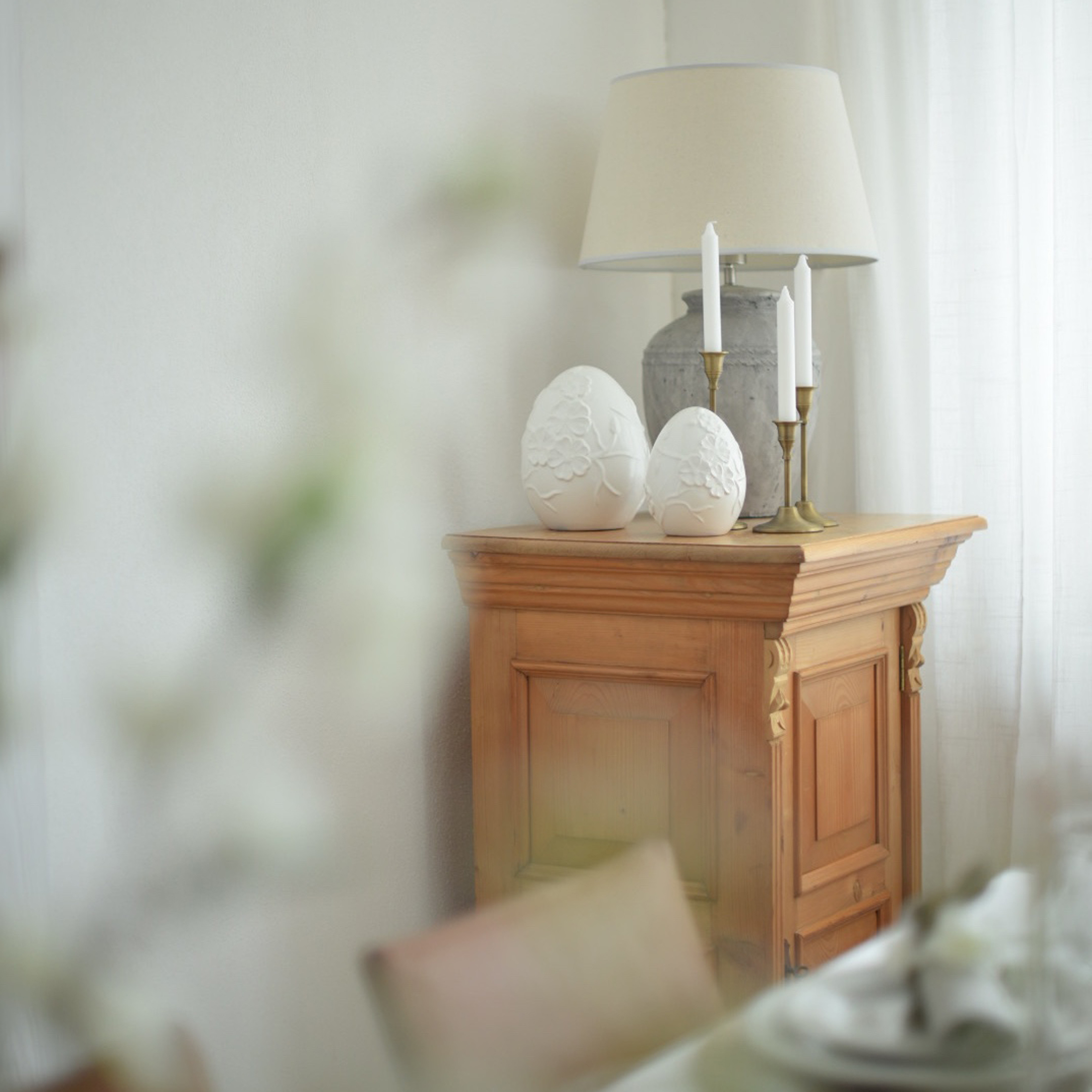 Mueble de madera con lámpara, velas y decoraciones de cerámica blanca en forma de huevos en interior luminoso