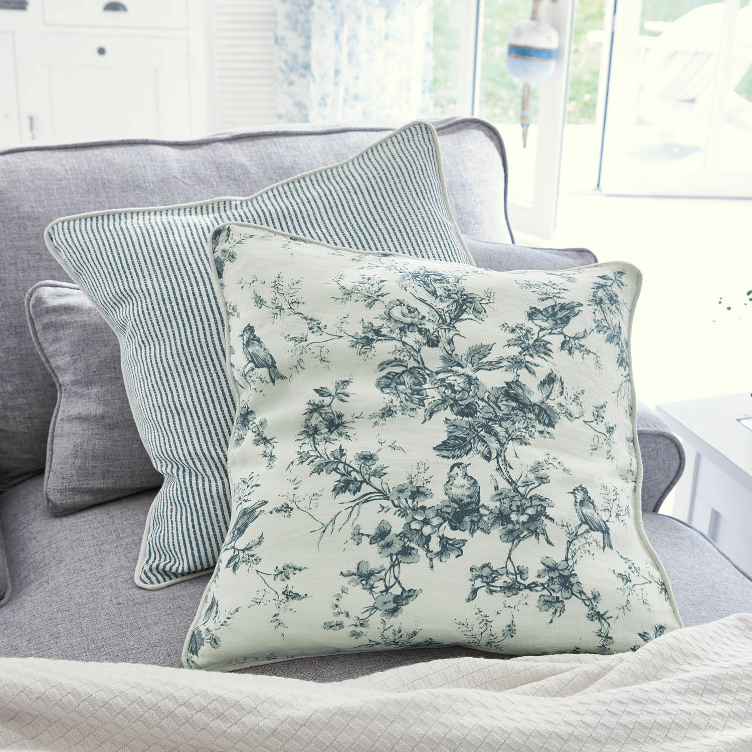 Set de 2 cojines Emilie Cojín decorativo reversible de algodón con estampados florales y rayas azules sobre sofá gris