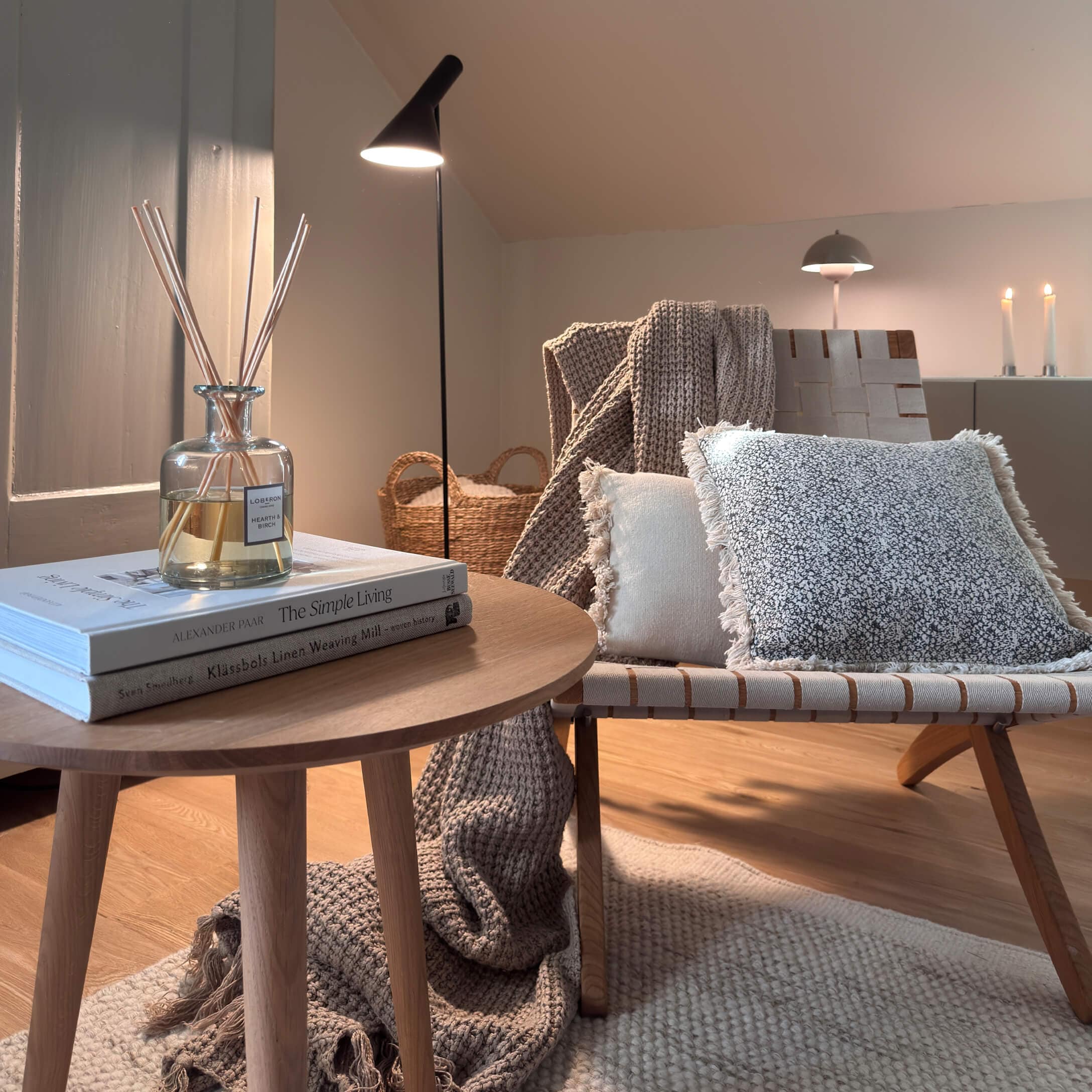 Rincón acogedor con mesa de madera, lámpara y cojines suaves en tonos naturales para ambiente cálido