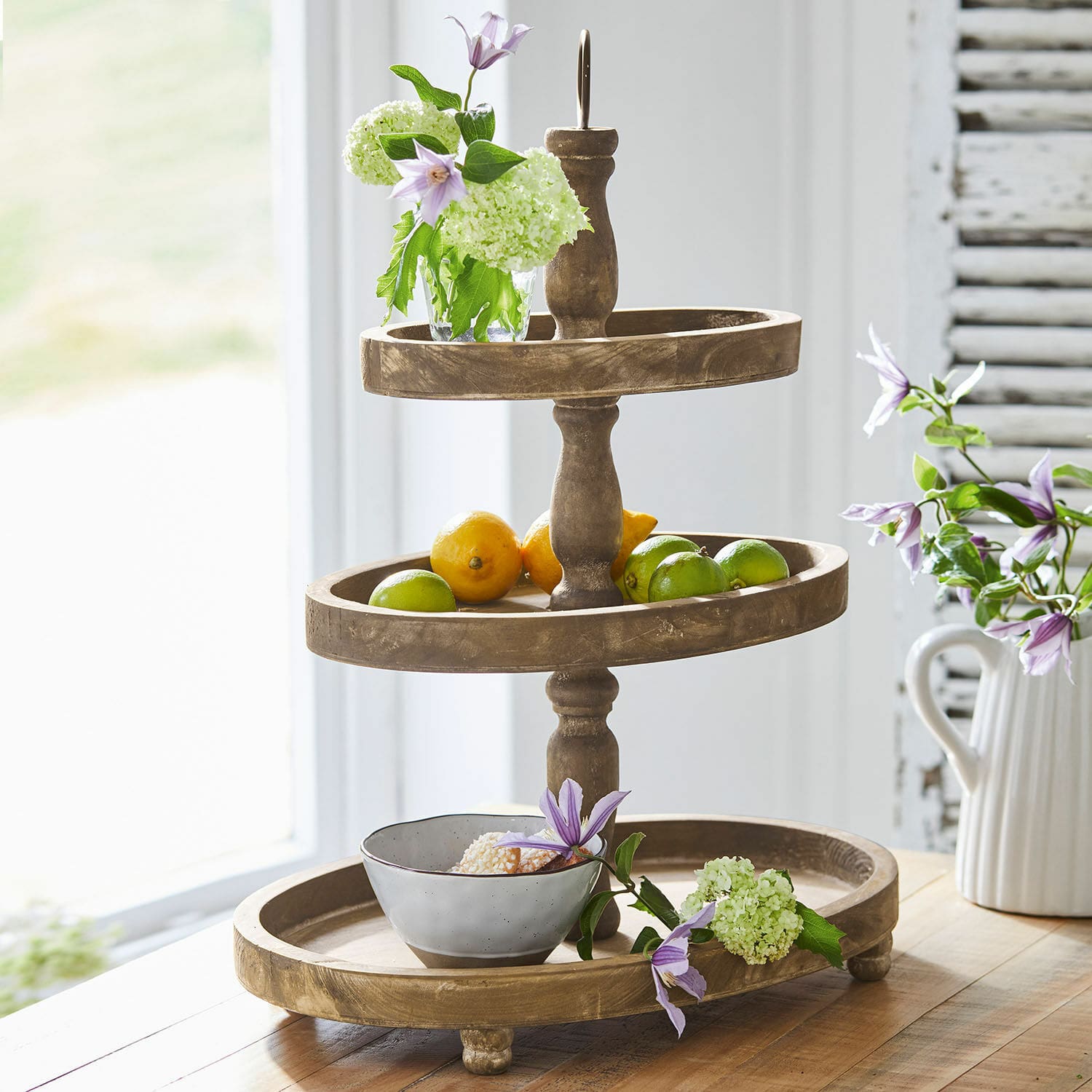 Bandeja de 3 niveles Olathe Frutero de madera de tres niveles con flores y frutas sobre mesa en interior luminoso