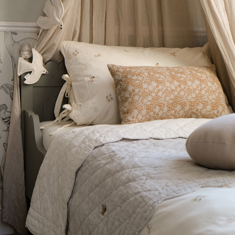 Cama acogedora con cojín beige con diseño floral y edredón acolchado claro de algodón