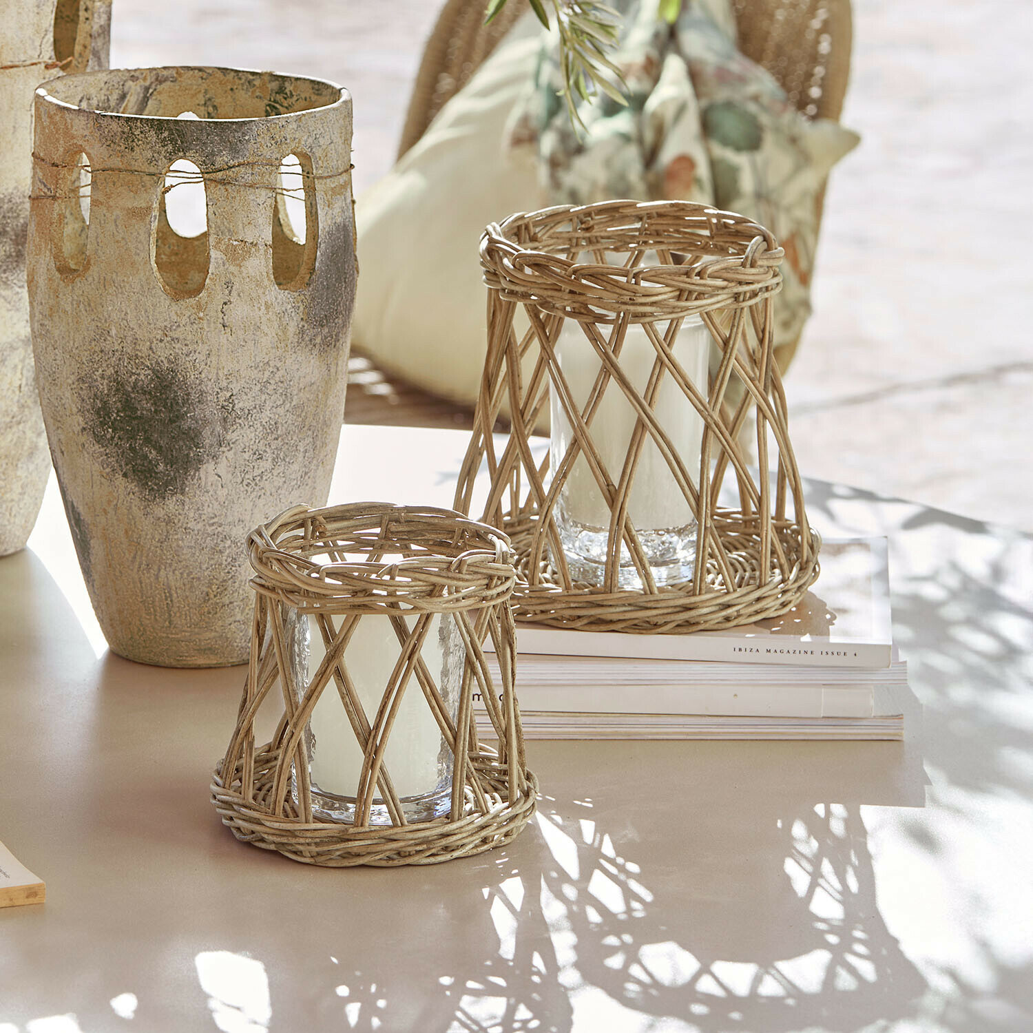 Set de 2 portavelas Melari Dos faroles de ratán natural con velas blancas sobre mesa clara en estilo bohemio