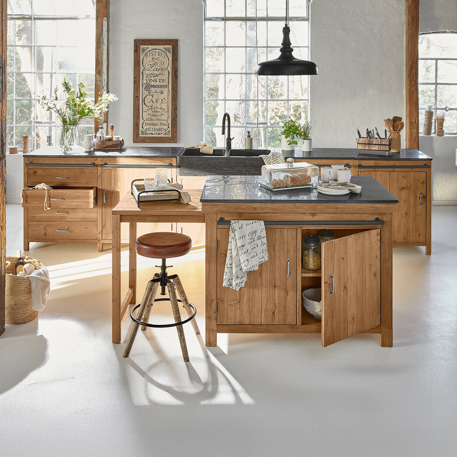 Cocina con muebles de madera y encimera negra, taburete alto y decoración luminosa