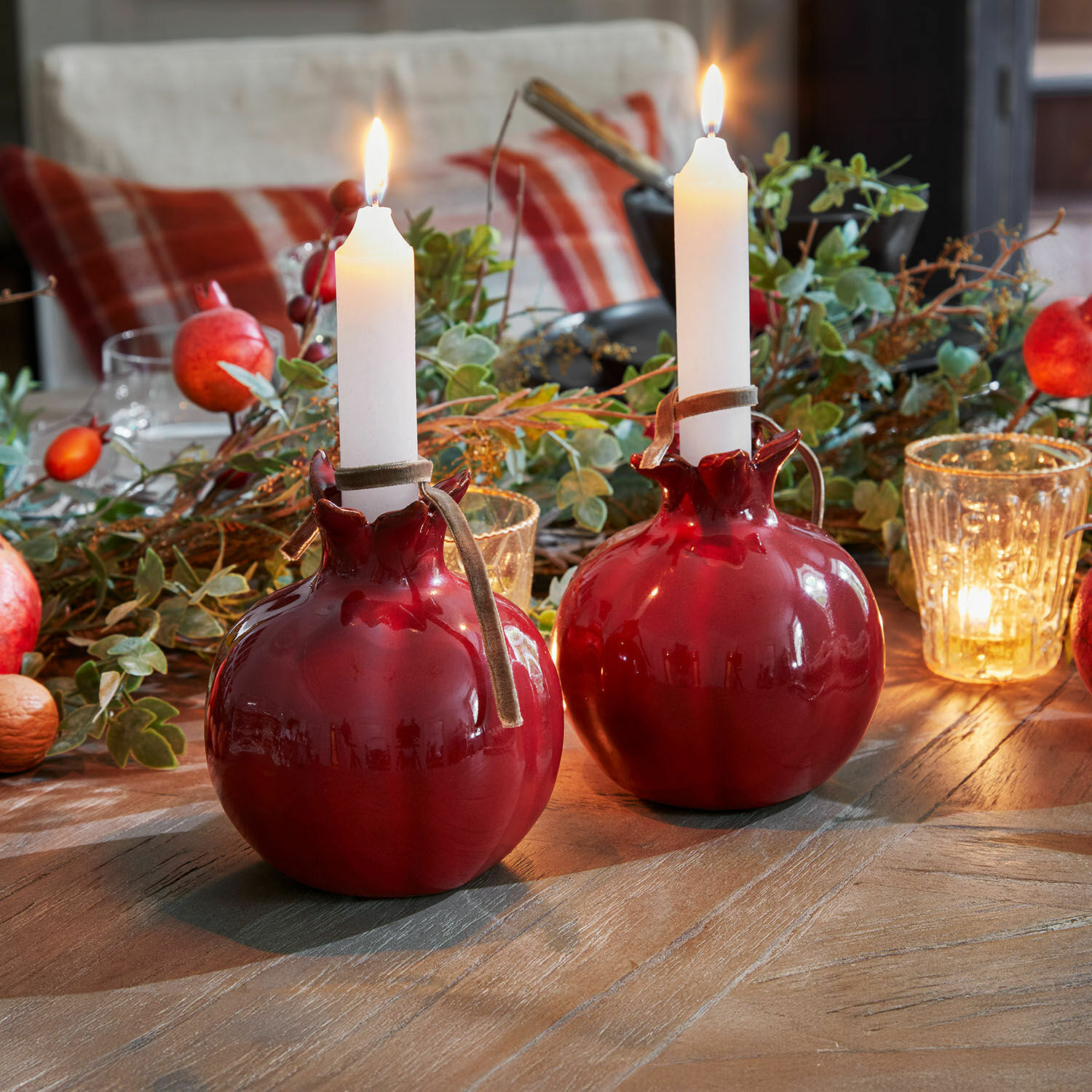 Set de 2 candeleros Karidah Dos candelabros de cerámica roja en forma de granada con velas blancas sobre mesa de madera decorada