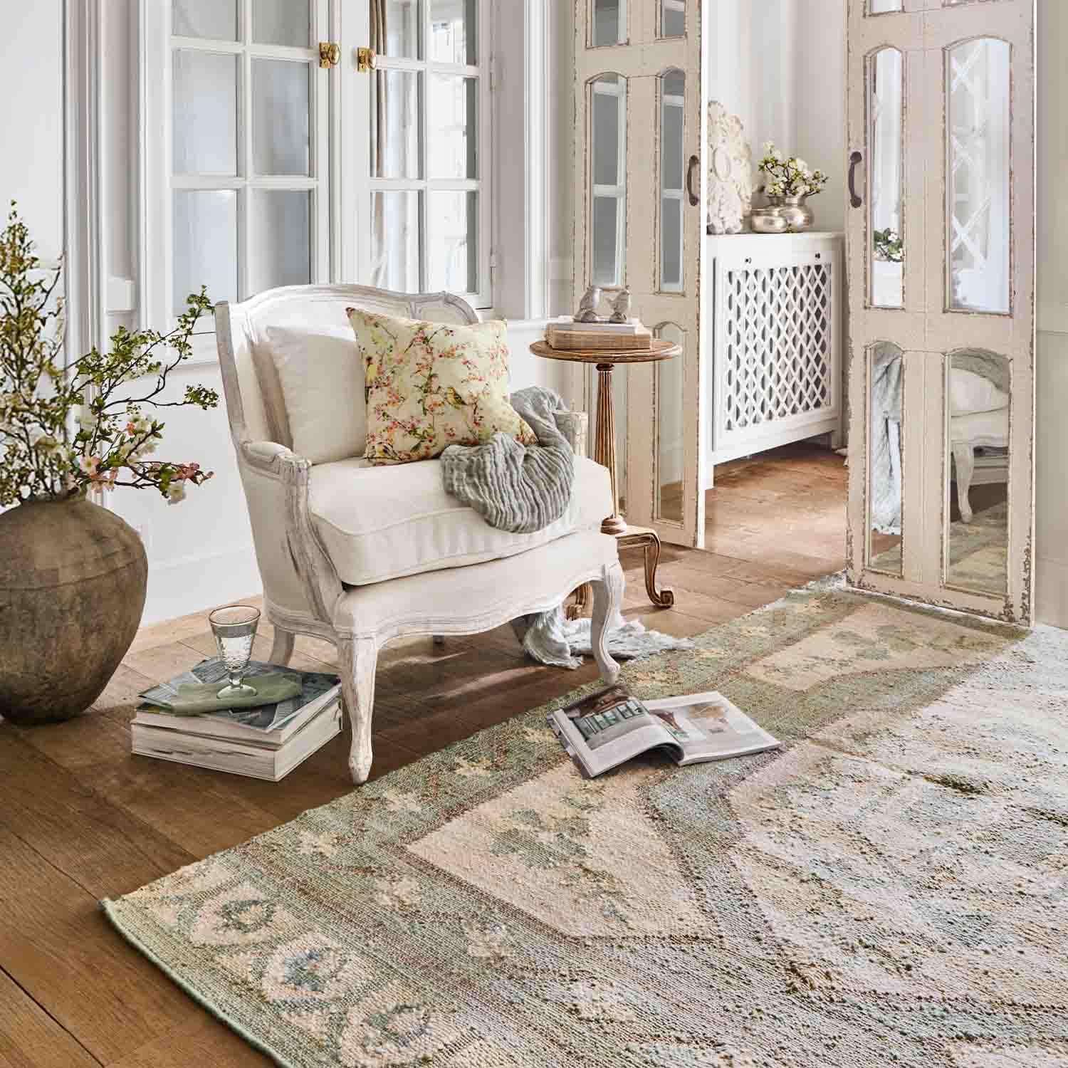 Sillón blanco de madera con cojín floral en sala luminosa con alfombra y espejo decorativo