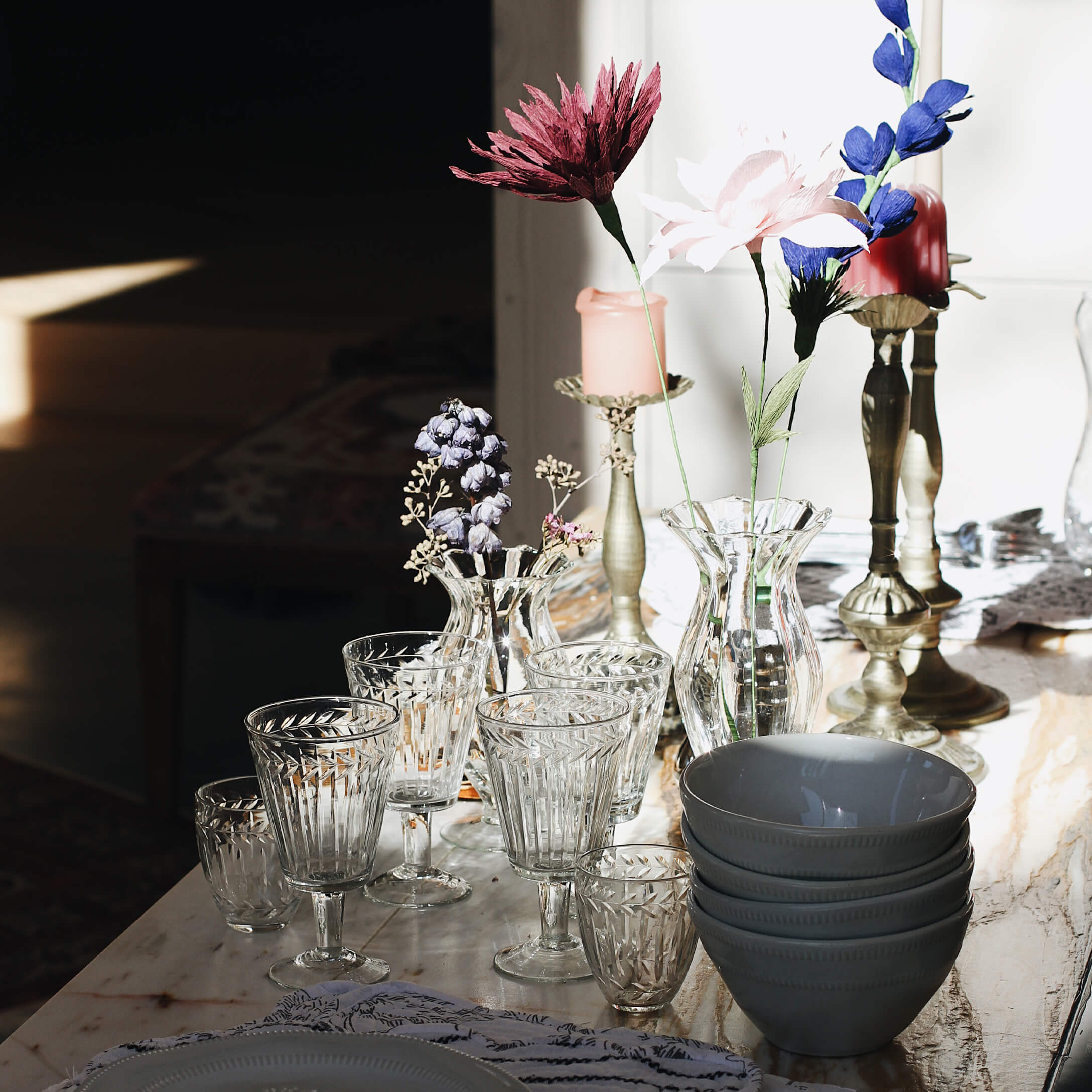 Conjunto de vasos y jarrones de vidrio transparente con flores y cuencos de cerámica gris sobre mesa de mármol